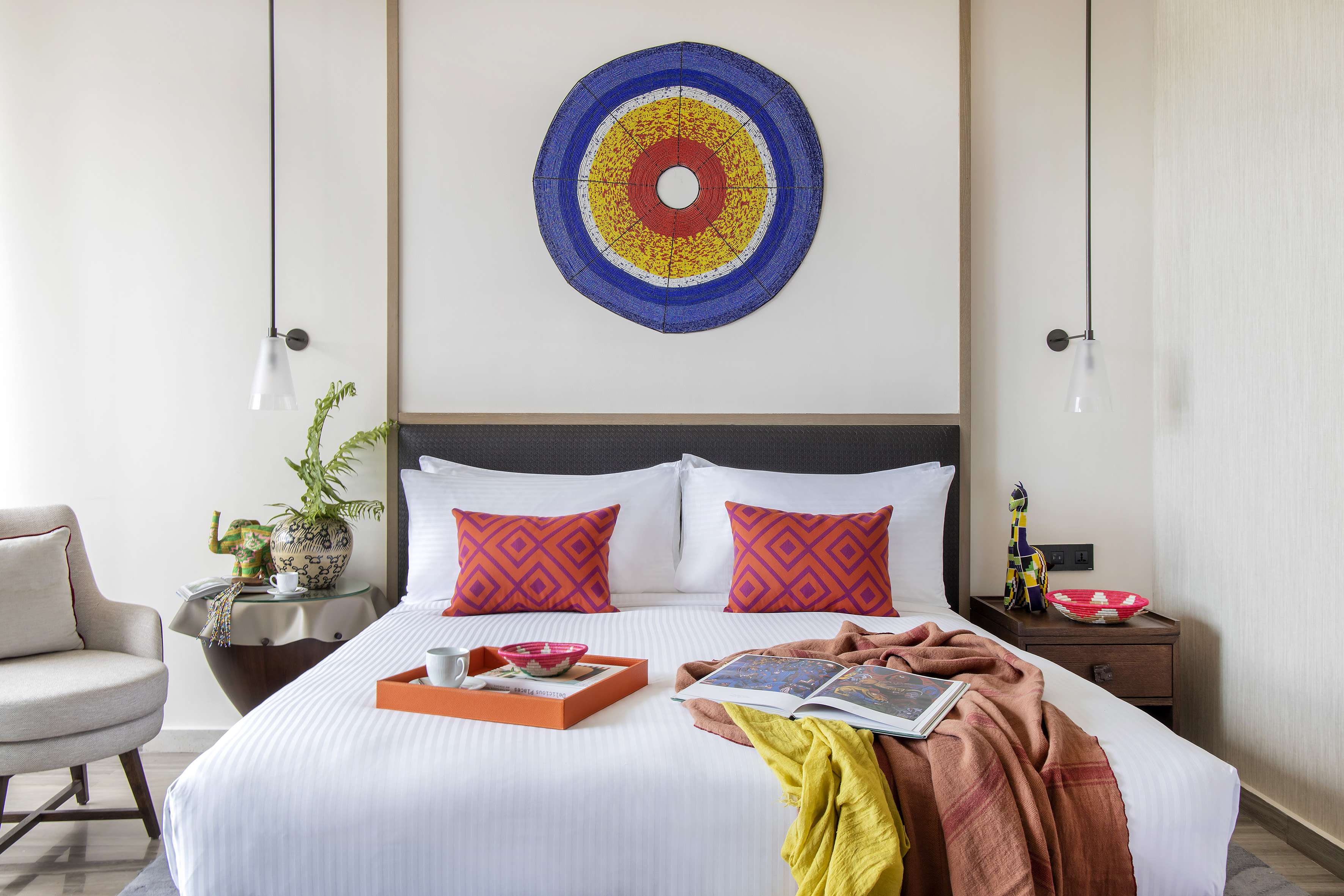 Stylish hotel bedroom with white bed, bold pillows, and colorful circular wall art.