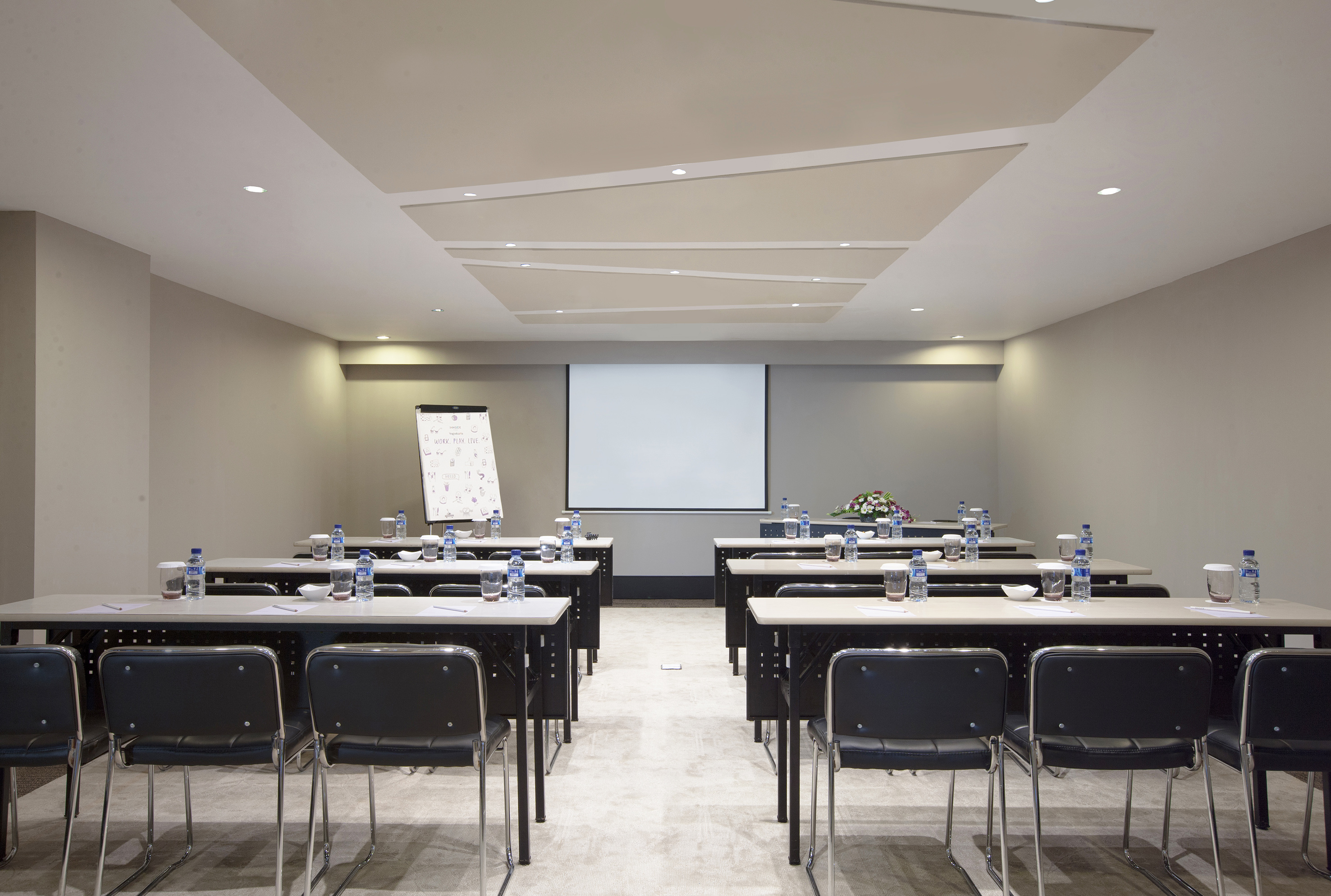 Meeting room with projector screen, flip chart, and classroom setup.