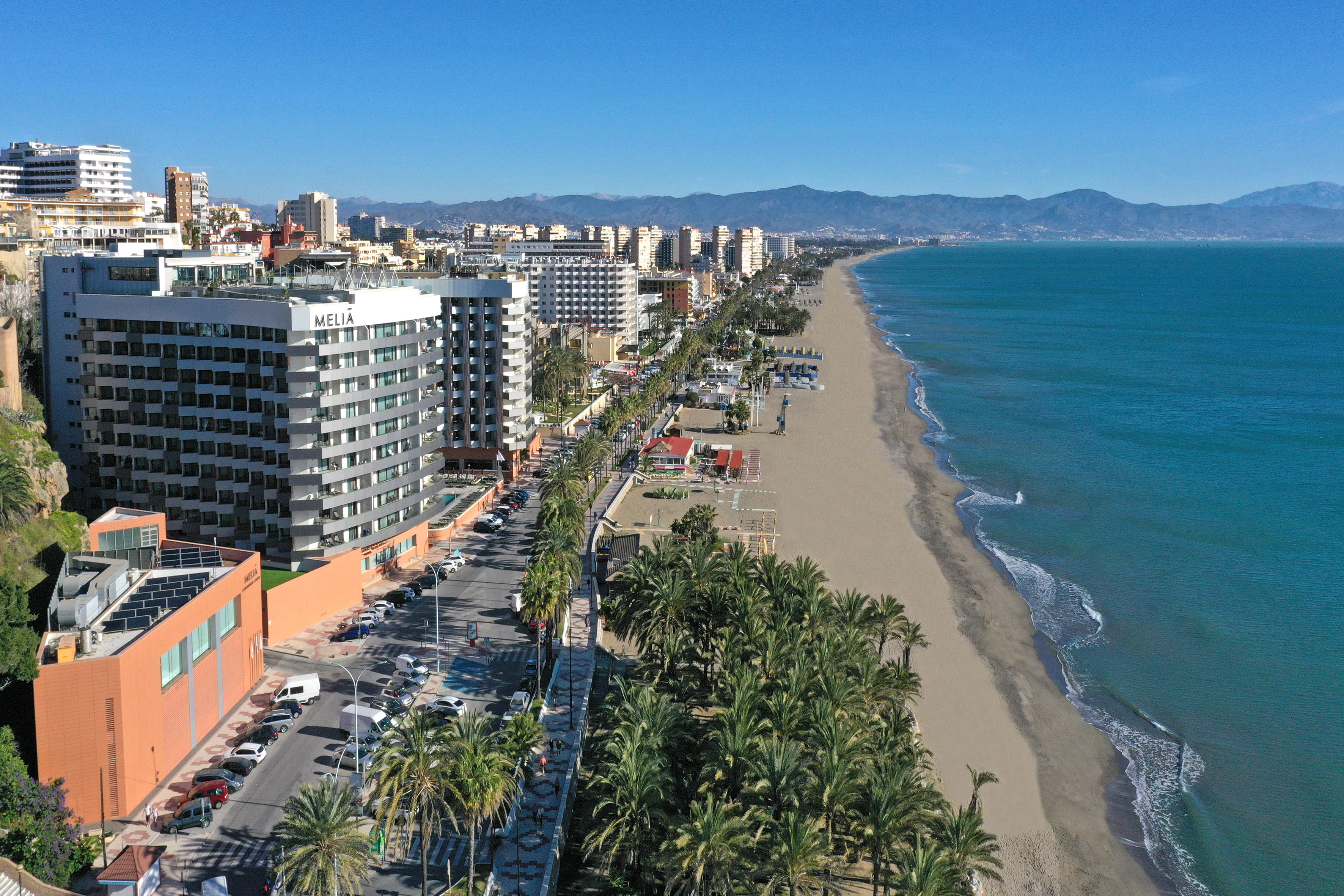 Sunny aerial view of Meliá hotel, beach, palm-lined street, and coastal city.