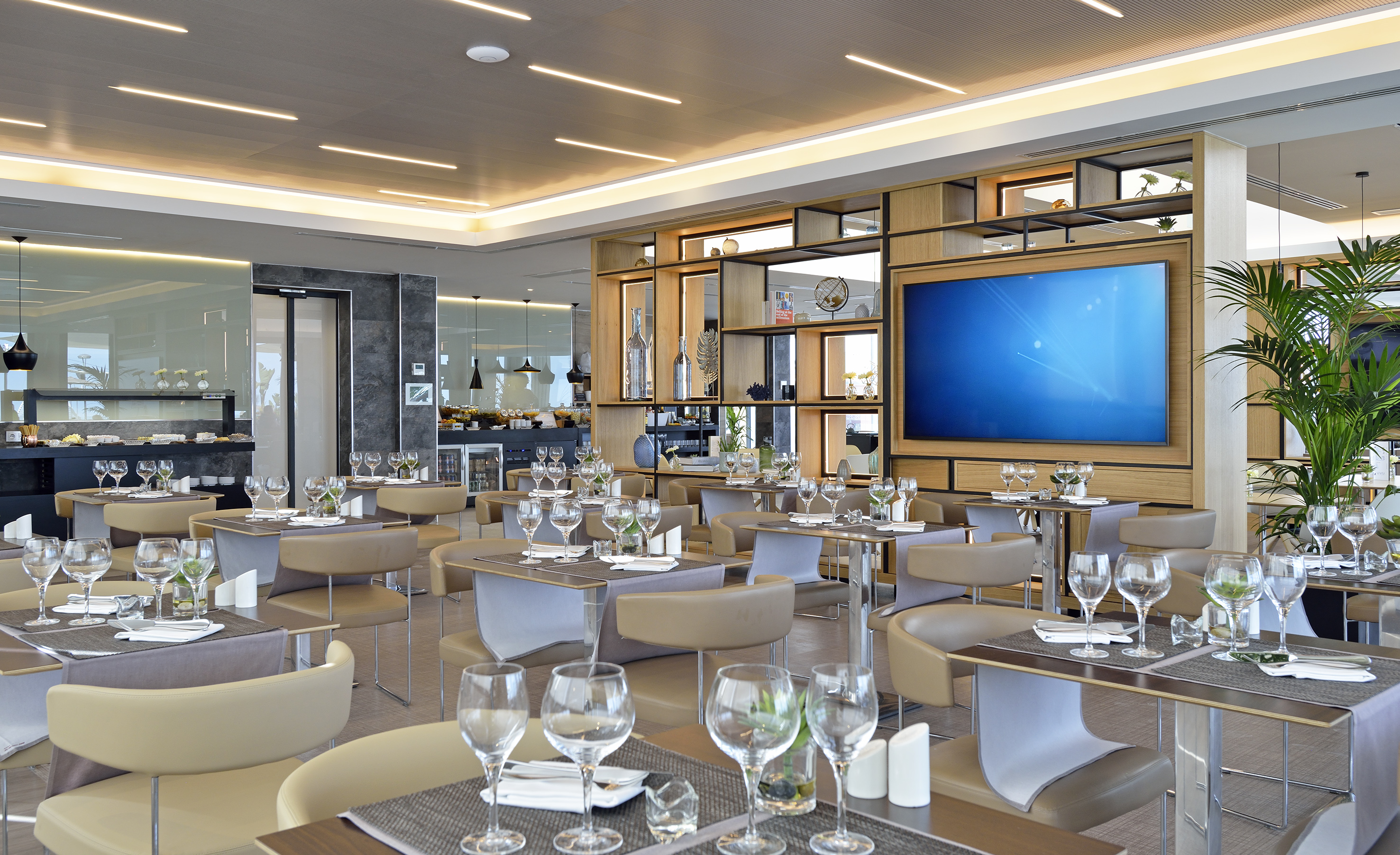 Elegant modern restaurant interior with set tables, large TV, and buffet area.