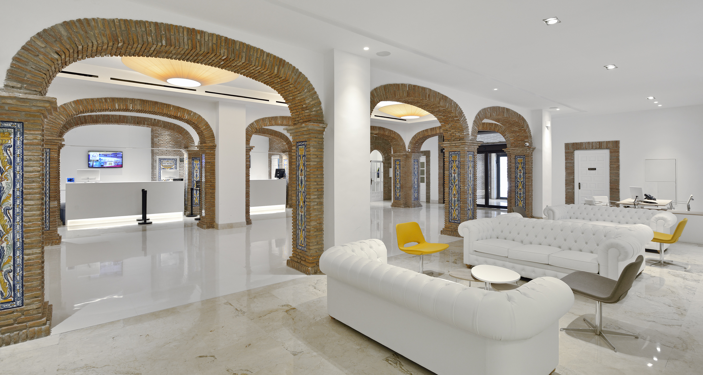 Hotel lobby with brick arches, tiled columns, white sofas, reception desk.
