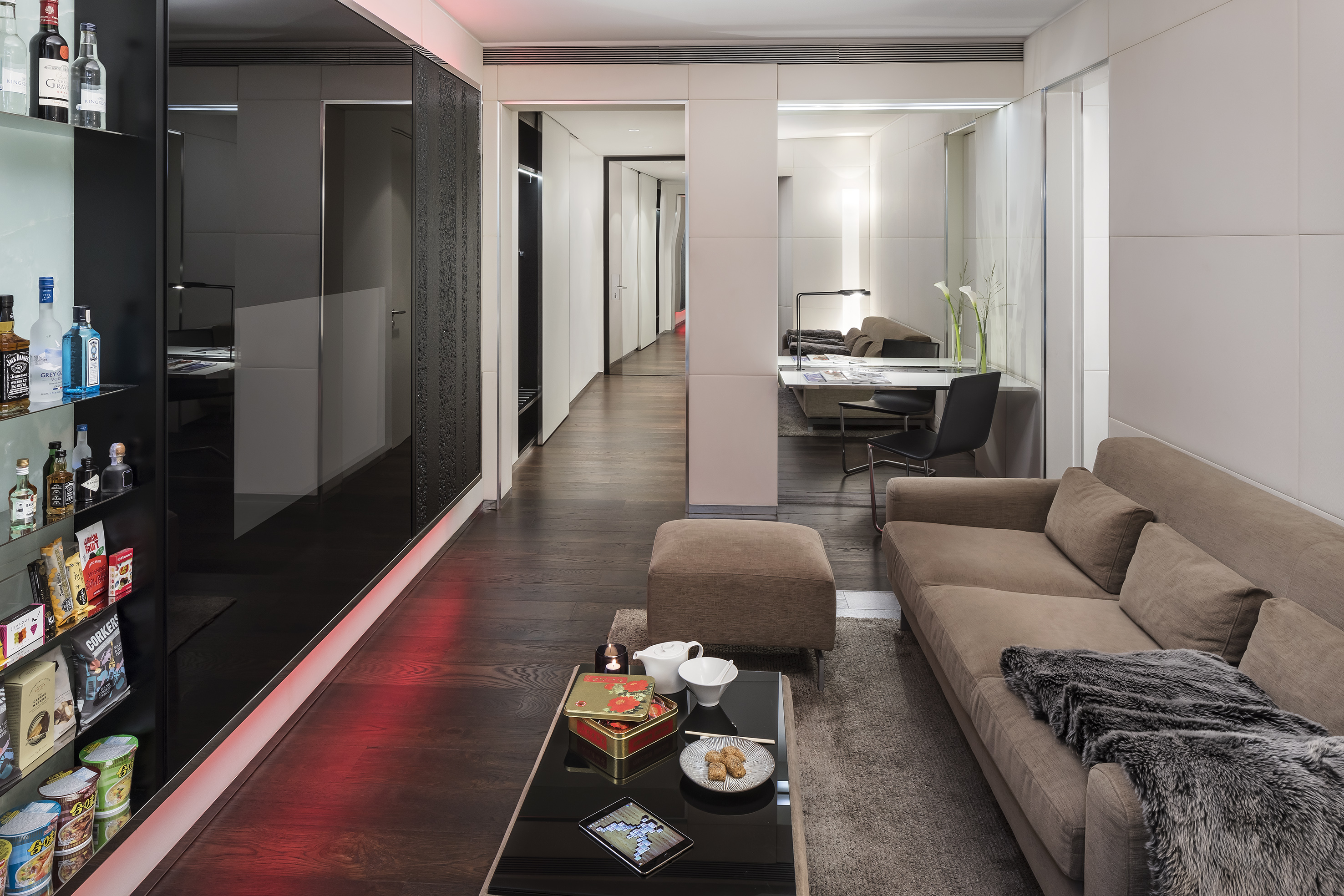 Modern luxury living room: sofa, coffee table, minibar, dark wood floor, red light.