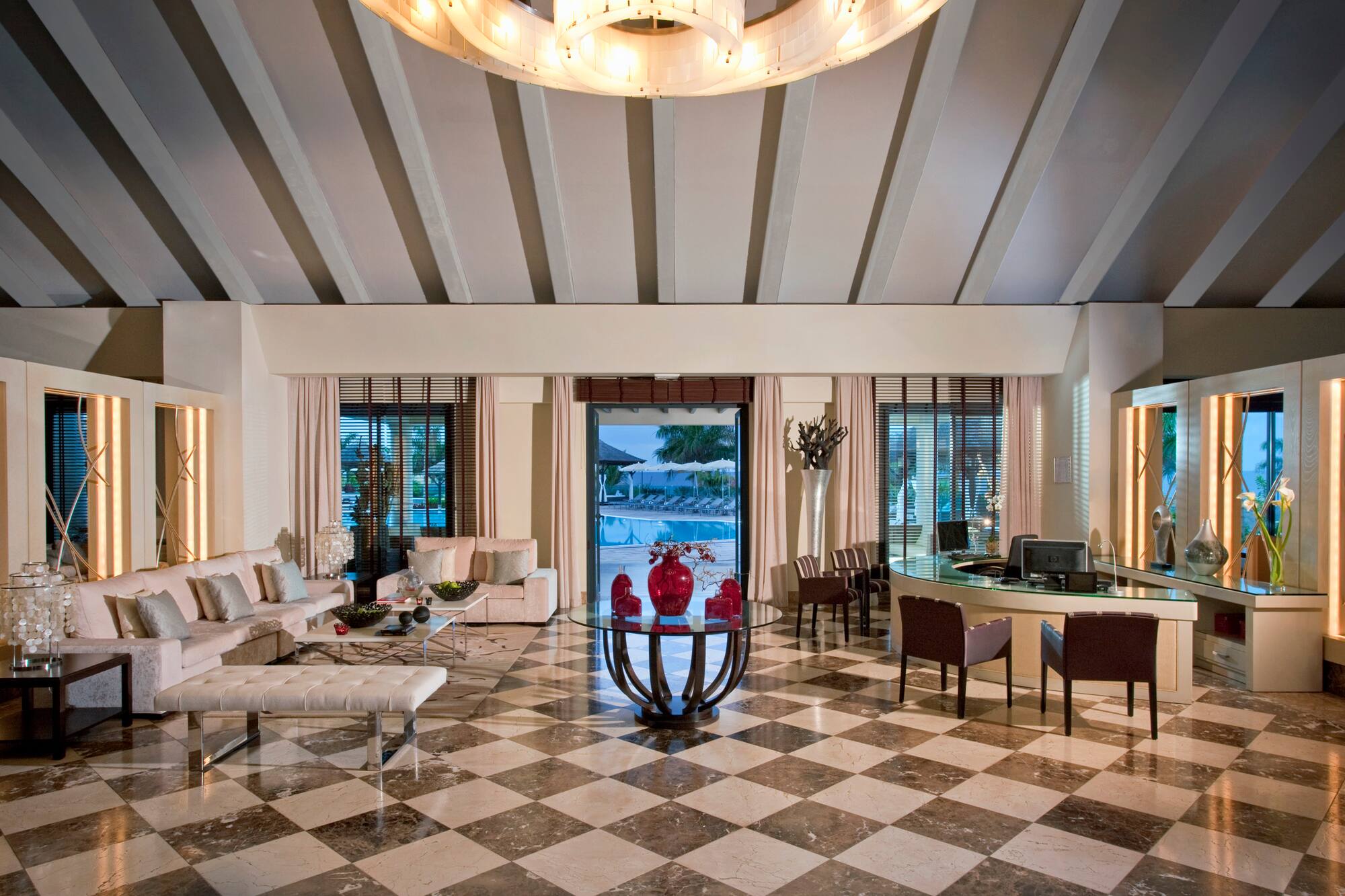 Luxury hotel reception with elegant seating, checkered floor, and swimming pool view.