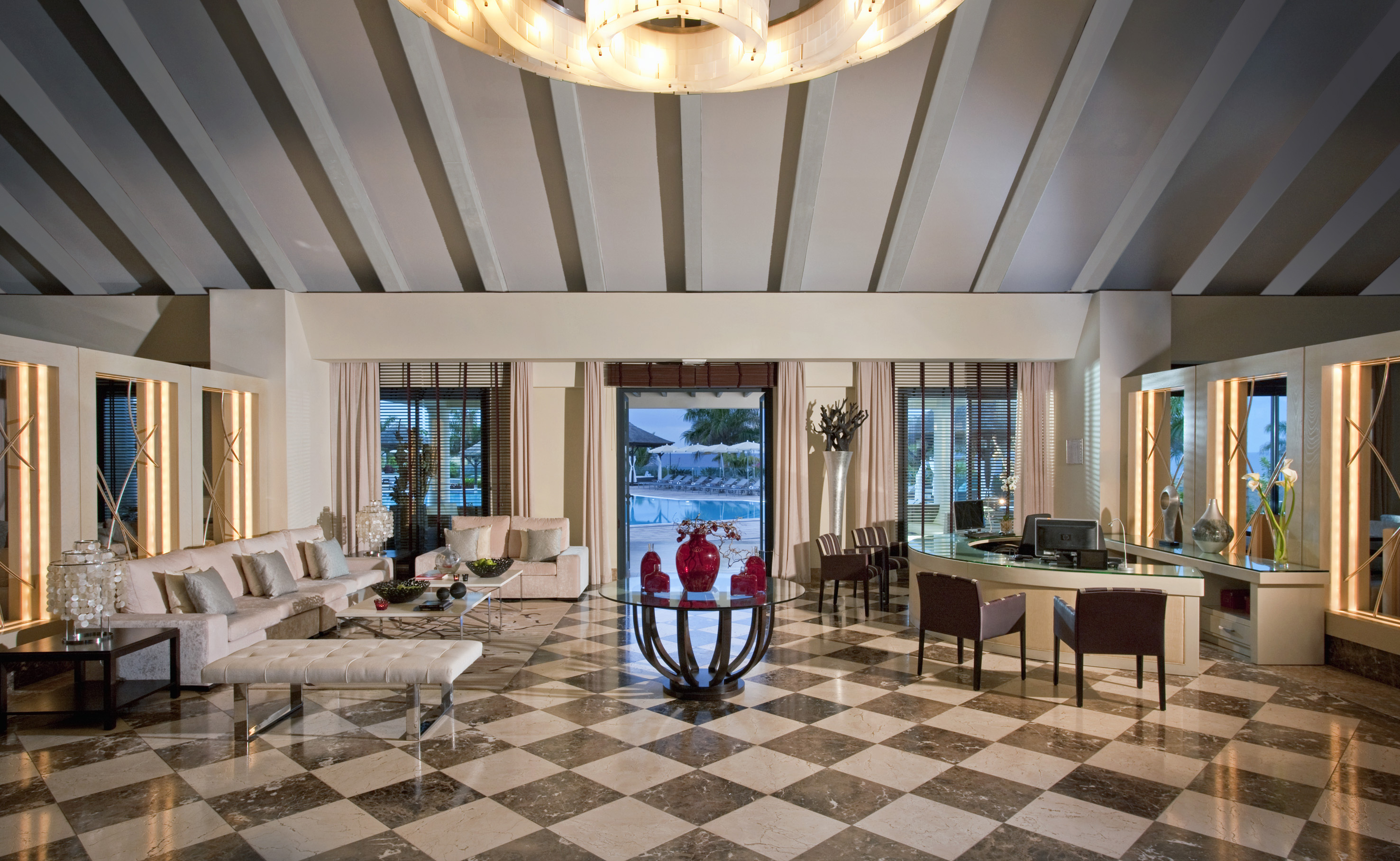 Luxury hotel reception with elegant seating, checkered floor, and swimming pool view.