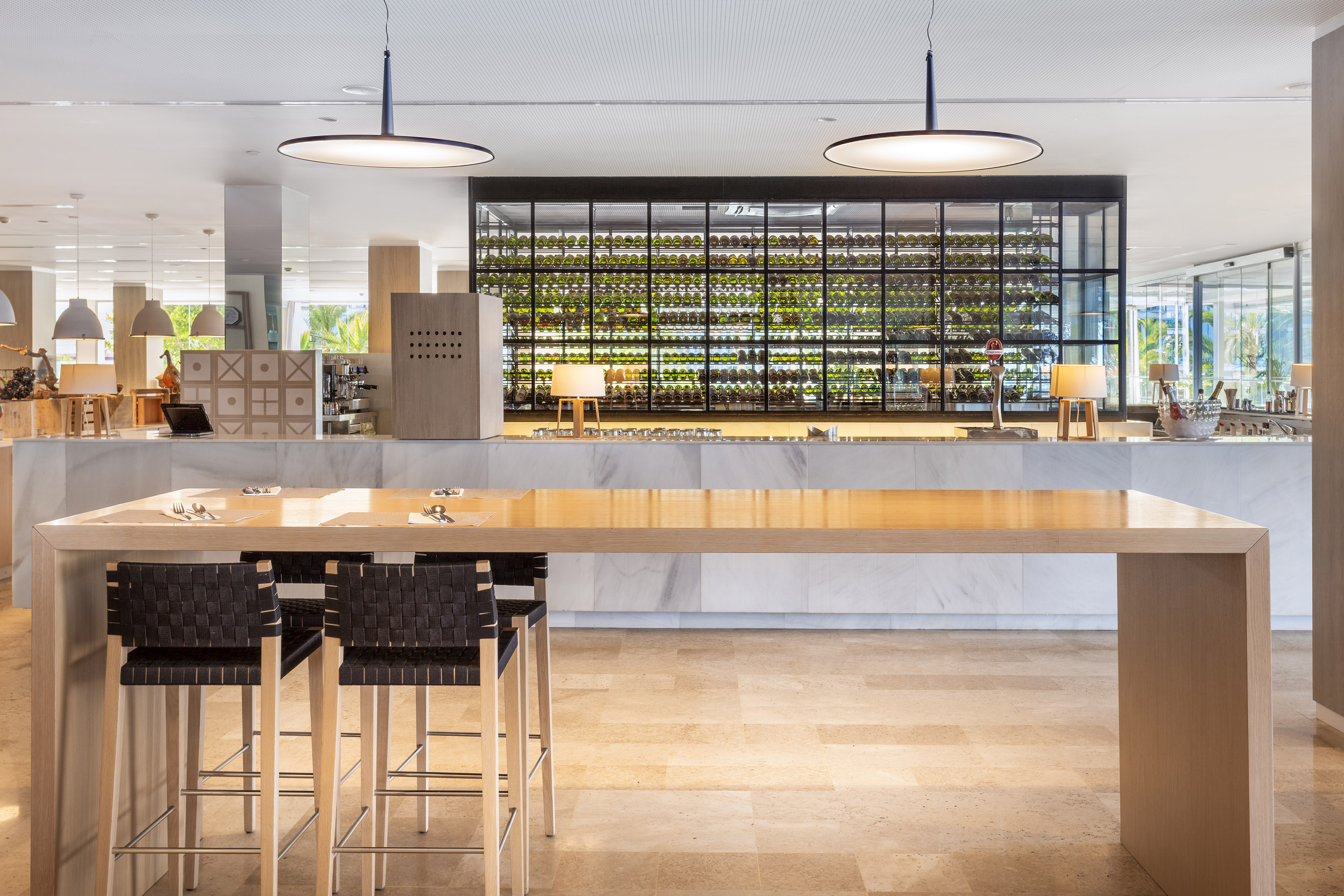 Modern hotel bar with large wine display, long wooden high table, and stools.