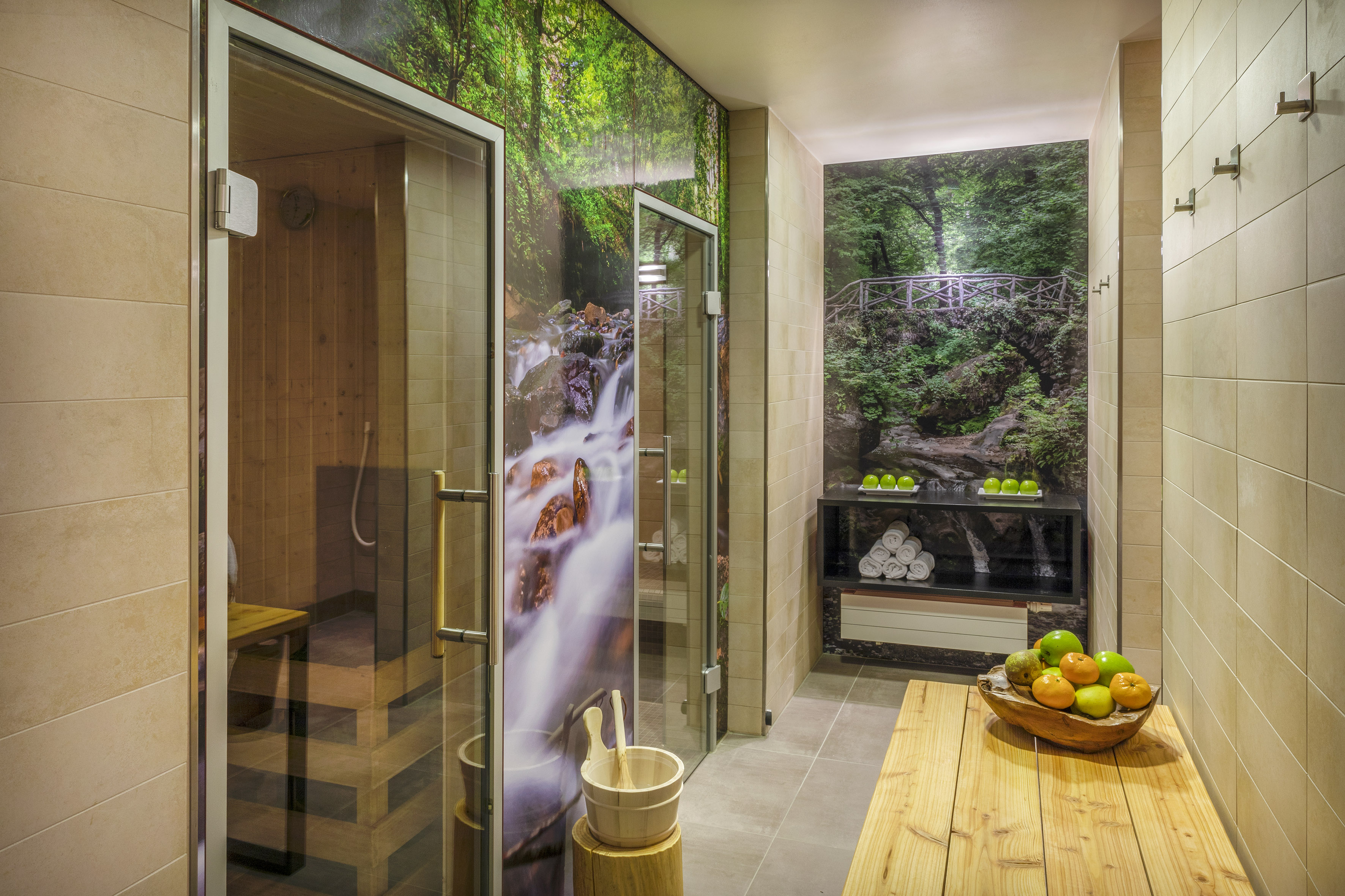 Spa sauna with forest and waterfall wall art, fruit, and towels.