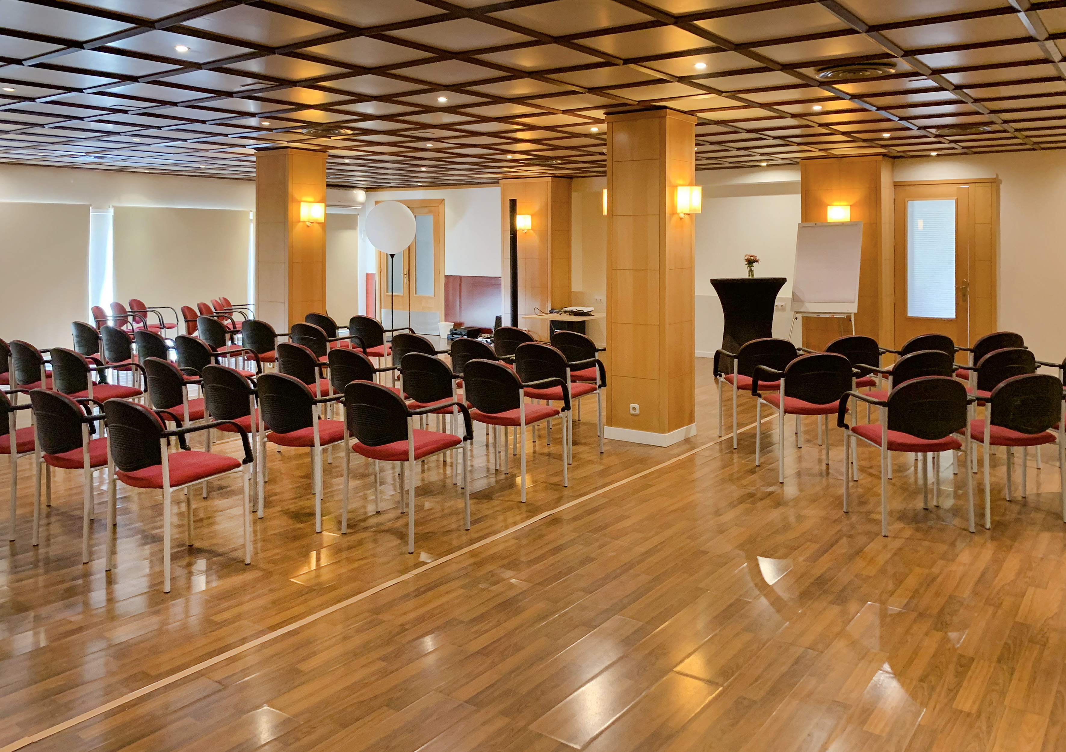 Empty meeting room with red chairs, wood floor, and presentation setup.