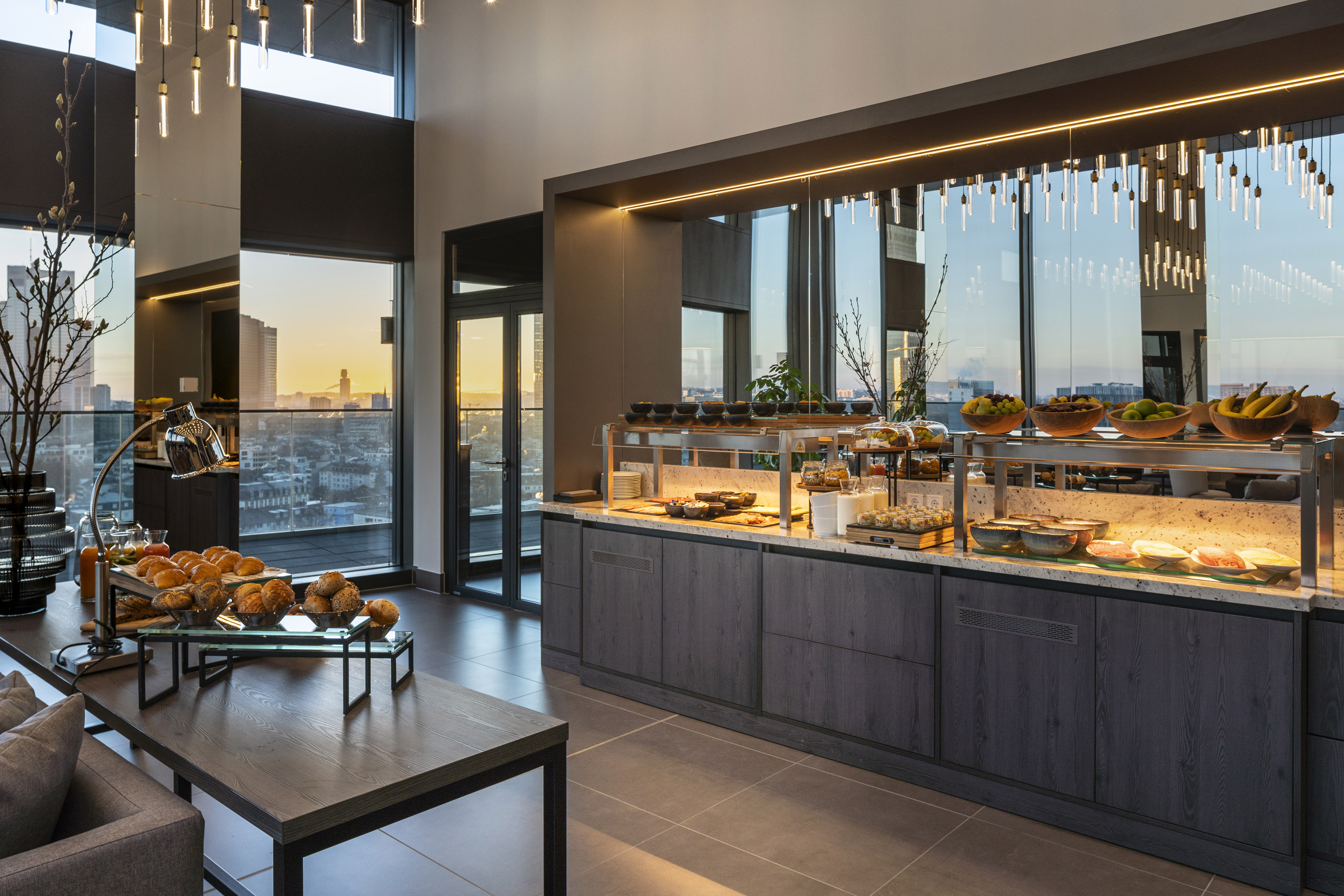 Modern hotel breakfast buffet with city skyline view at sunset.
