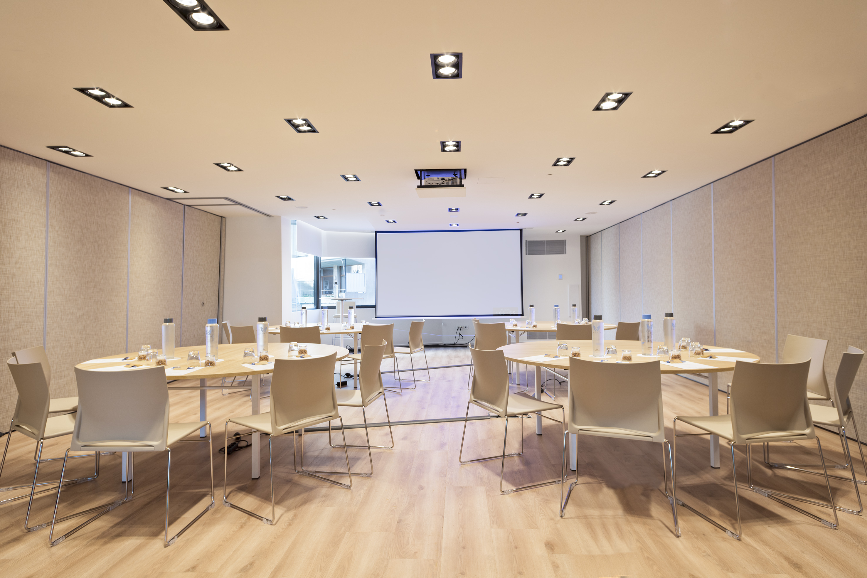 Modern conference room with round tables, chairs, and projector screen.