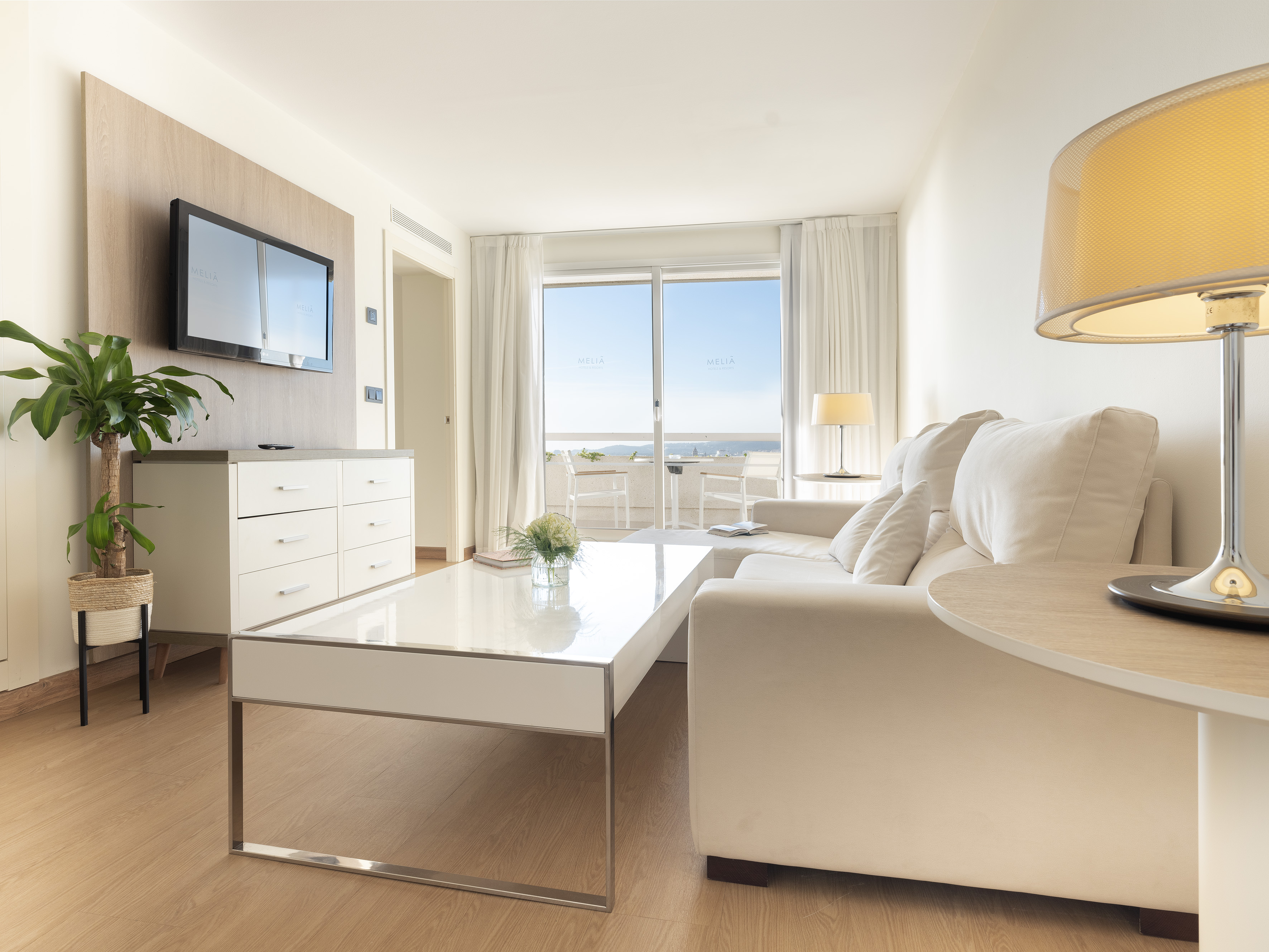 Modern hotel suite living room with white sofa and sea view balcony.