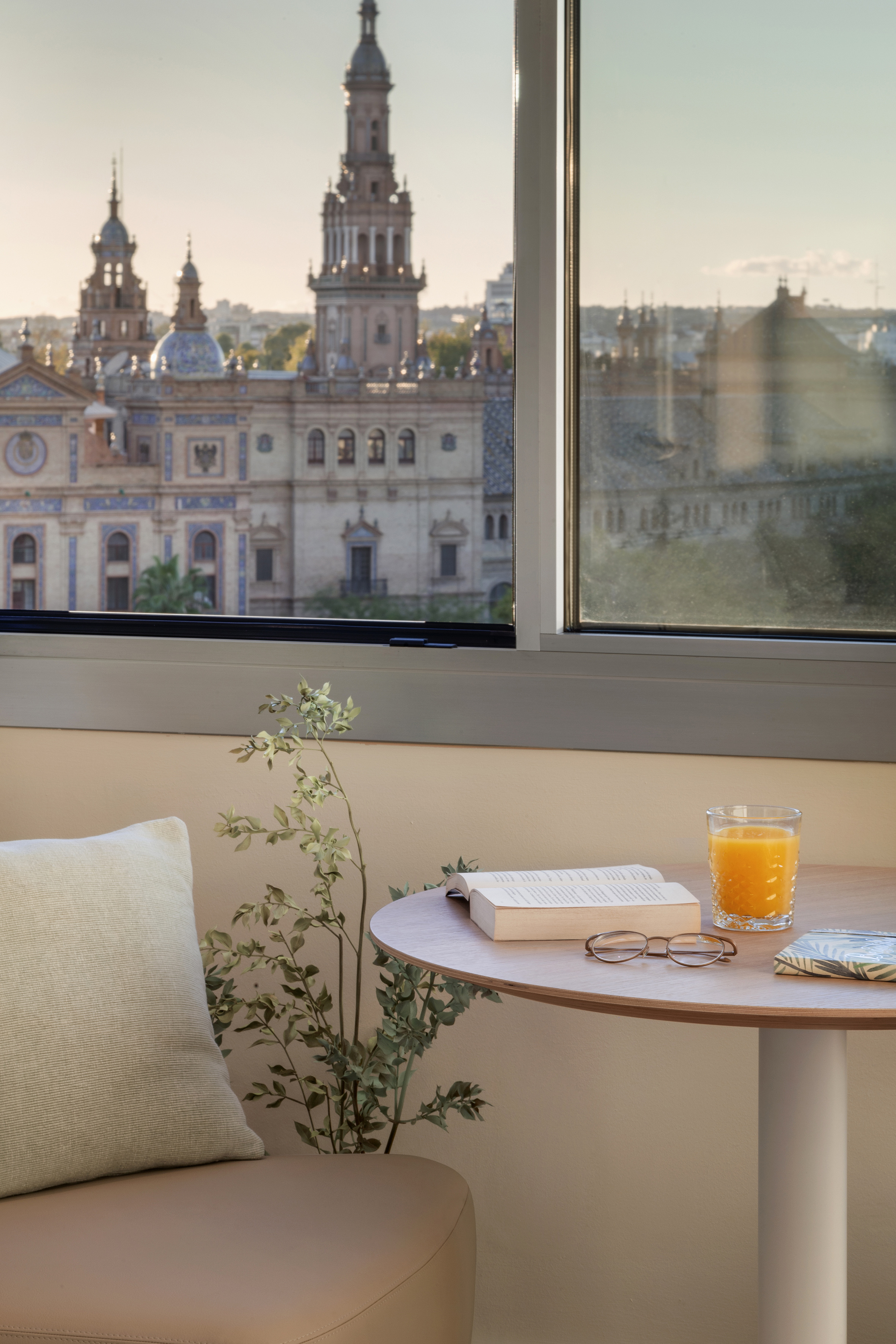 Cozy window view of Seville's Plaza de España with a book and juice.