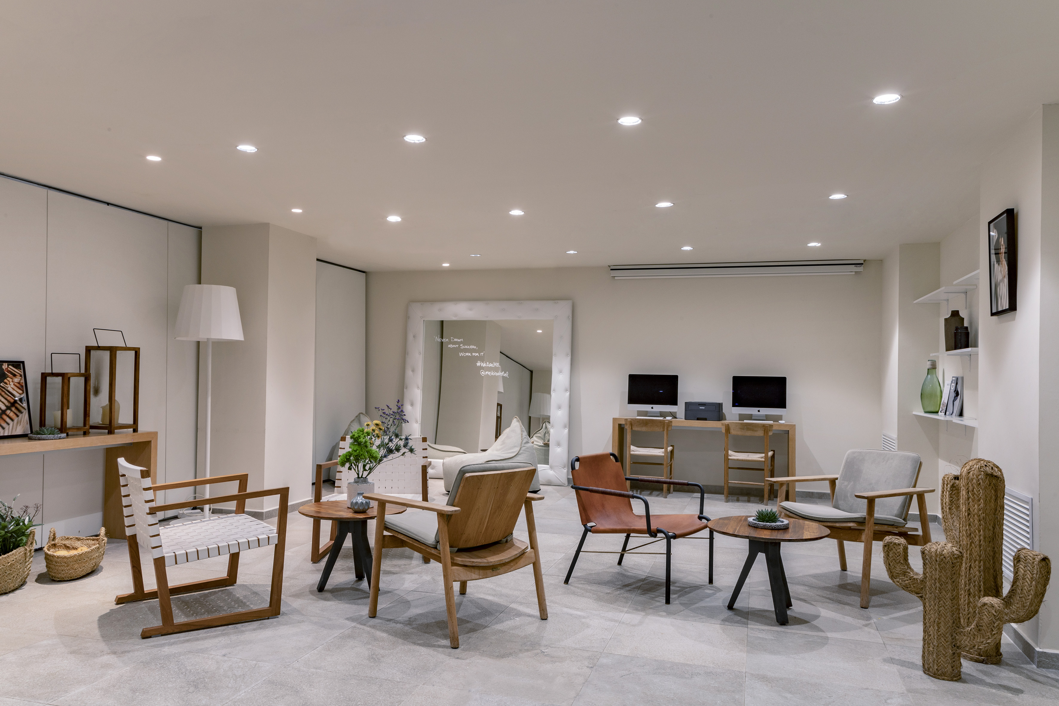 Modern hotel lounge: armchairs, coffee tables, computers, and large mirror.