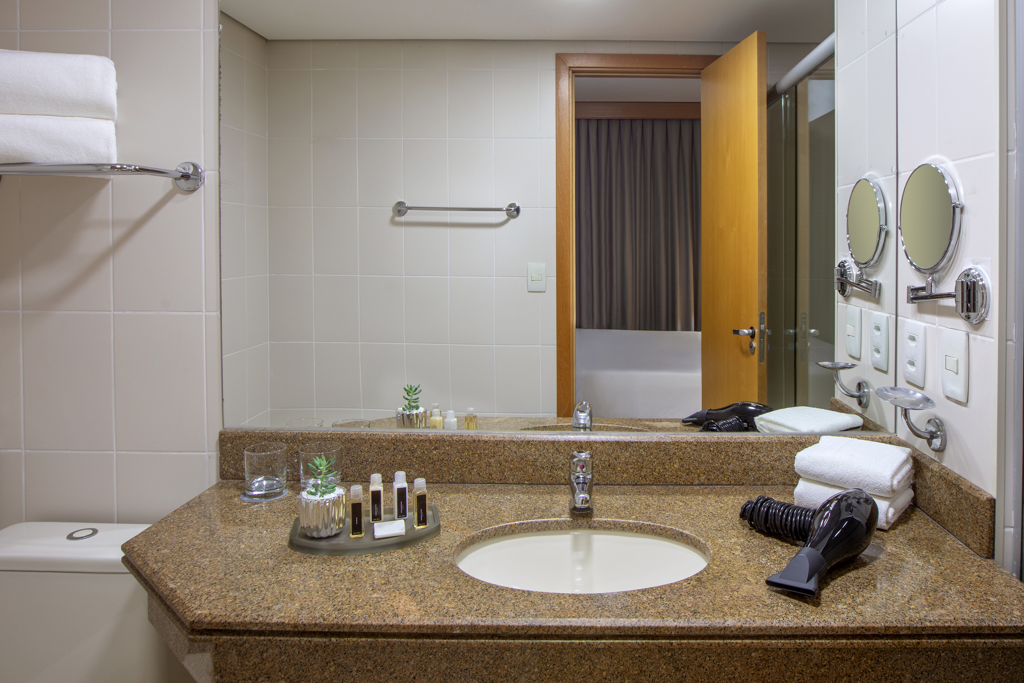 Hotel bathroom with granite vanity, sink, mirror, toiletries, and hairdryer.
