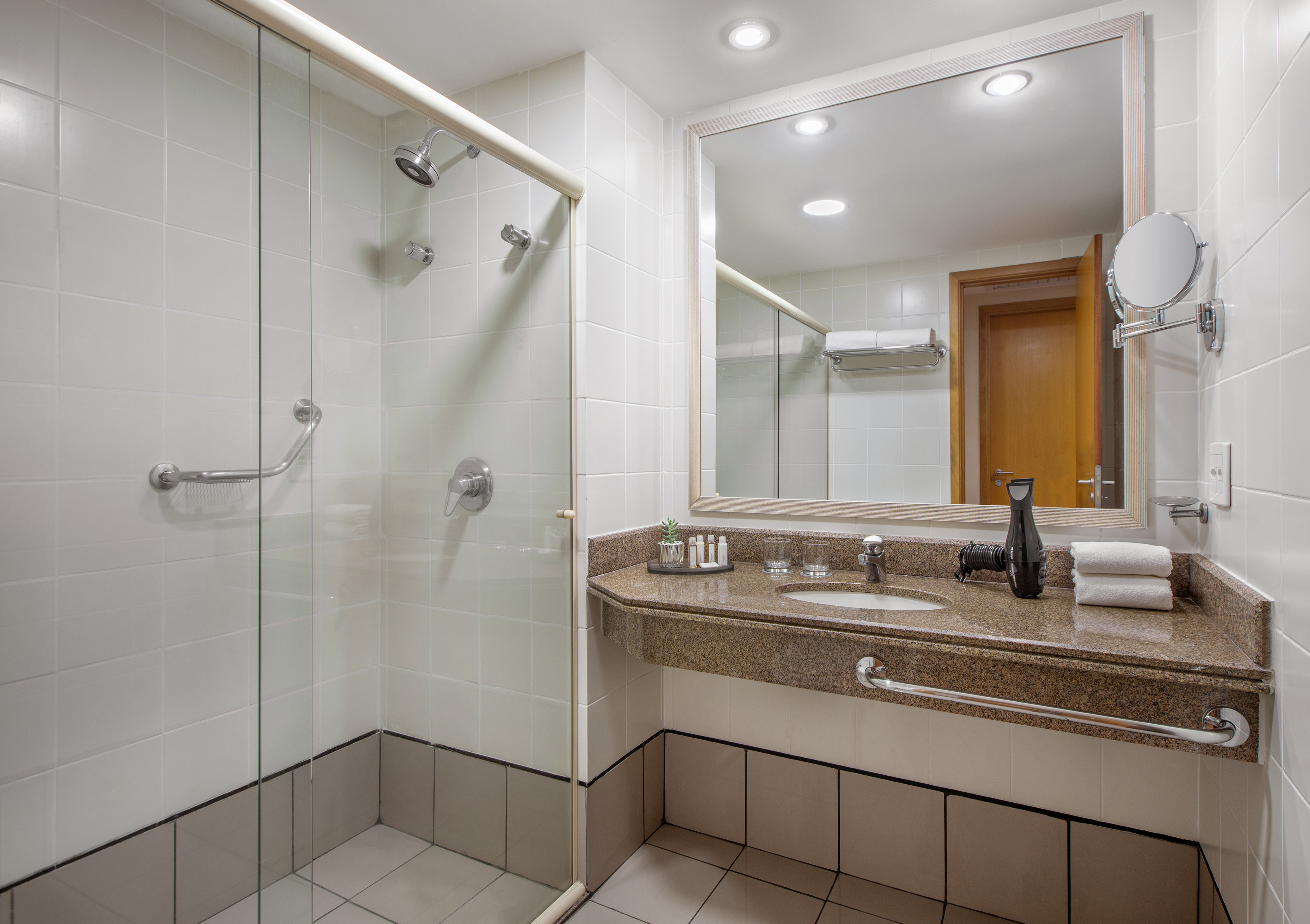 Hotel bathroom with accessible shower, granite vanity, mirror, and toiletries.