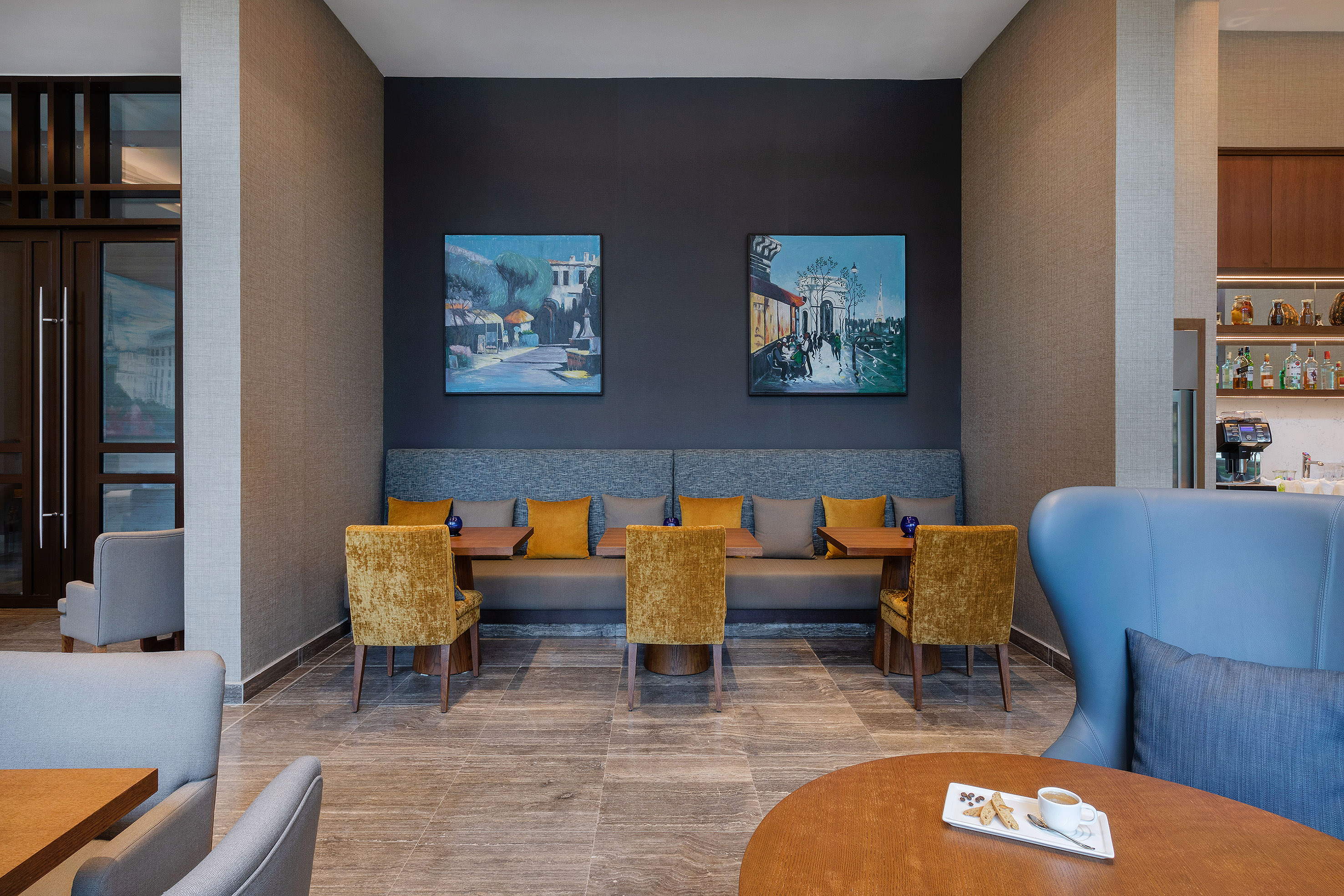 Modern cafe interior with booth seating, gold chairs, wall art, and coffee station.