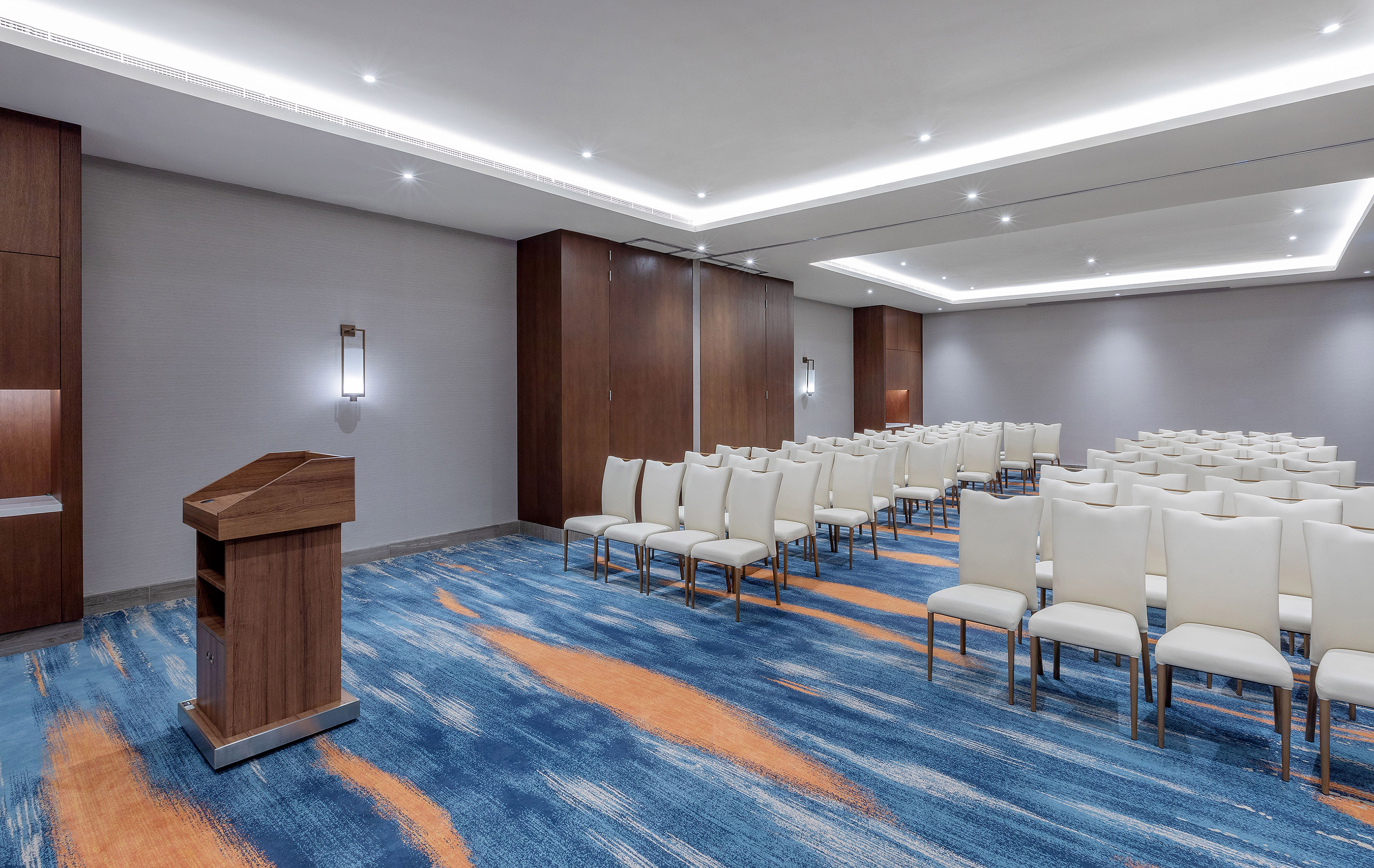 Modern empty conference room with white chairs, wooden podium, blue carpet.