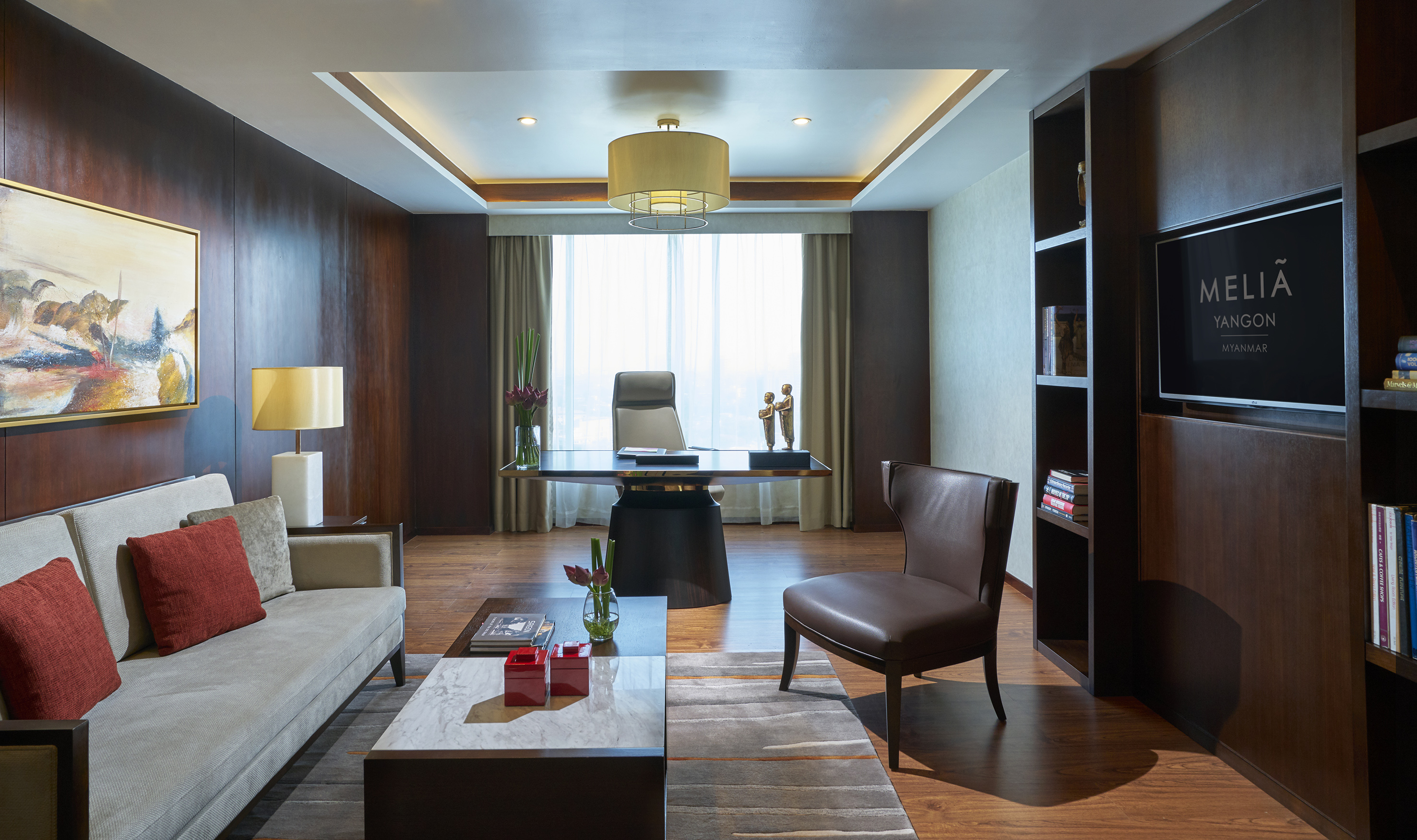 Modern Melia Yangon hotel suite with executive desk, sofa, and TV.