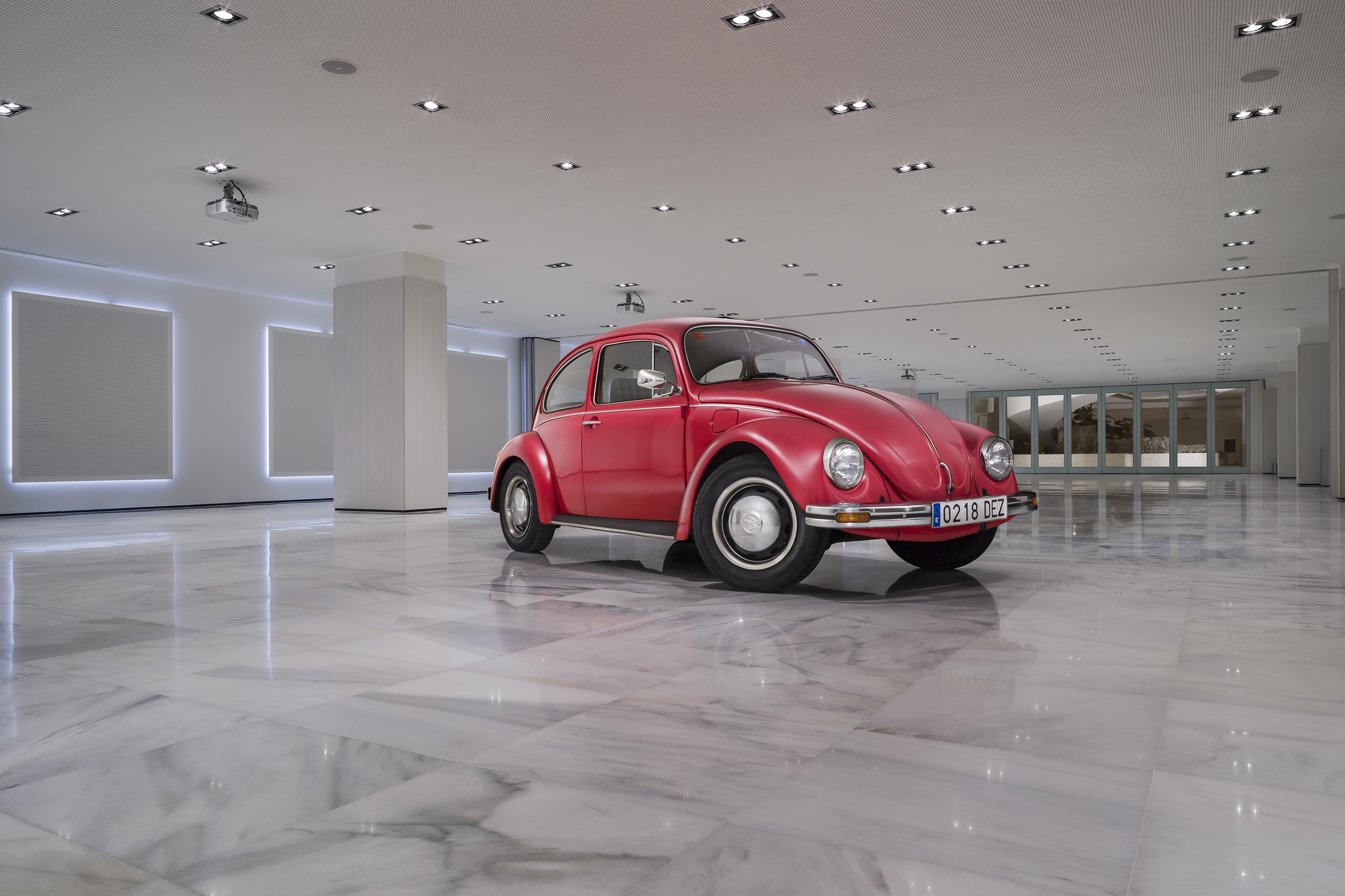 Red classic Volkswagen Beetle on polished marble floor, modern showroom.