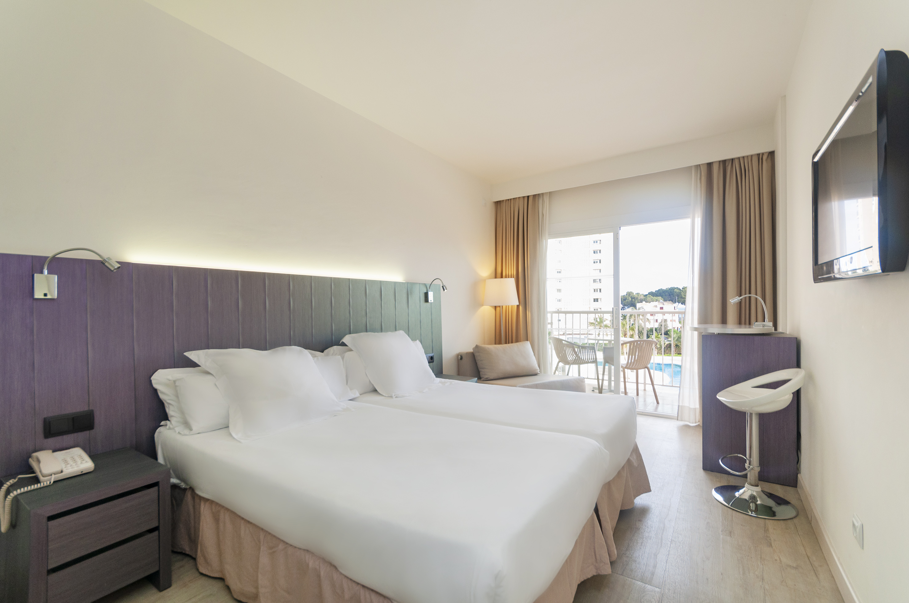 Bright hotel room with twin beds, private balcony, and poolside view.