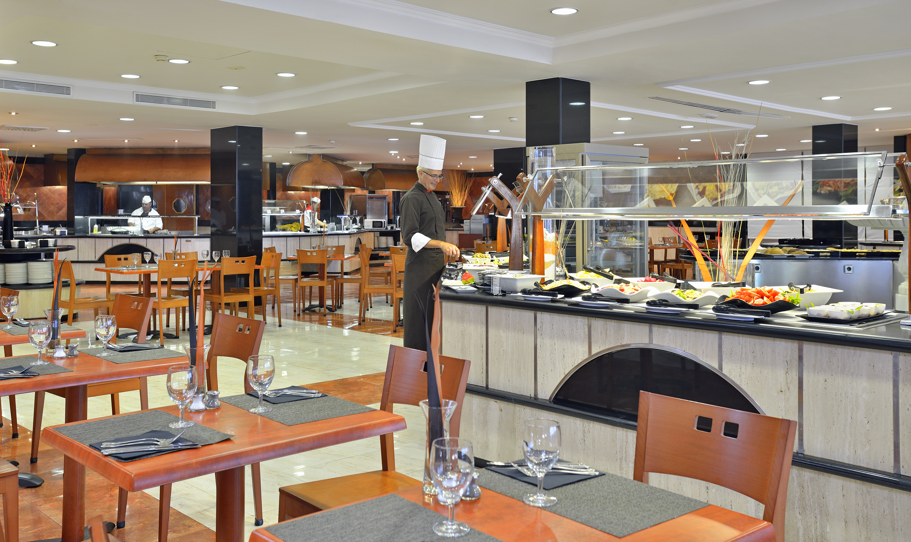 Hotel buffet restaurant with chef attending food display and set dining tables.