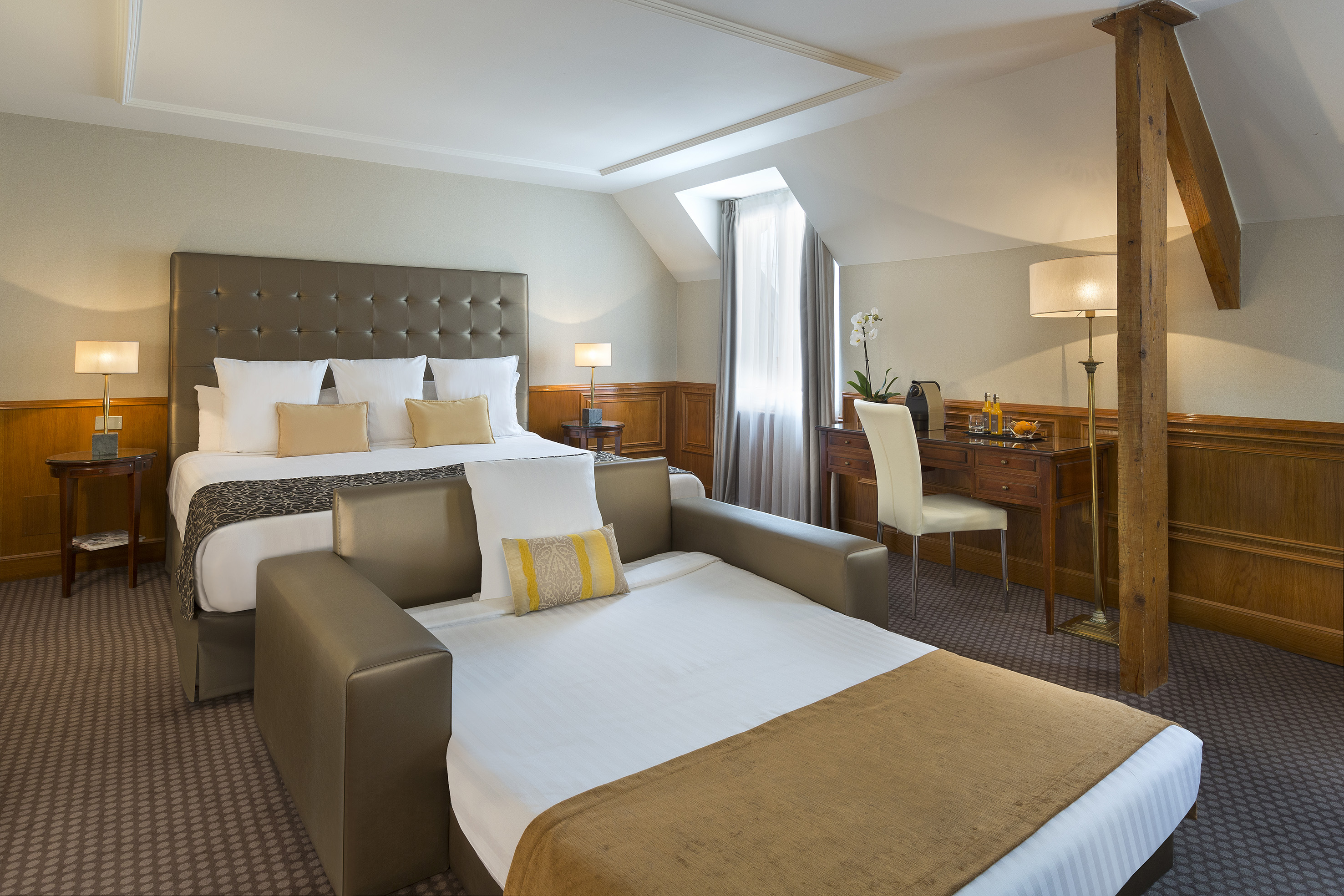 Hotel guest room with large bed, opened sofa bed, and wooden desk.