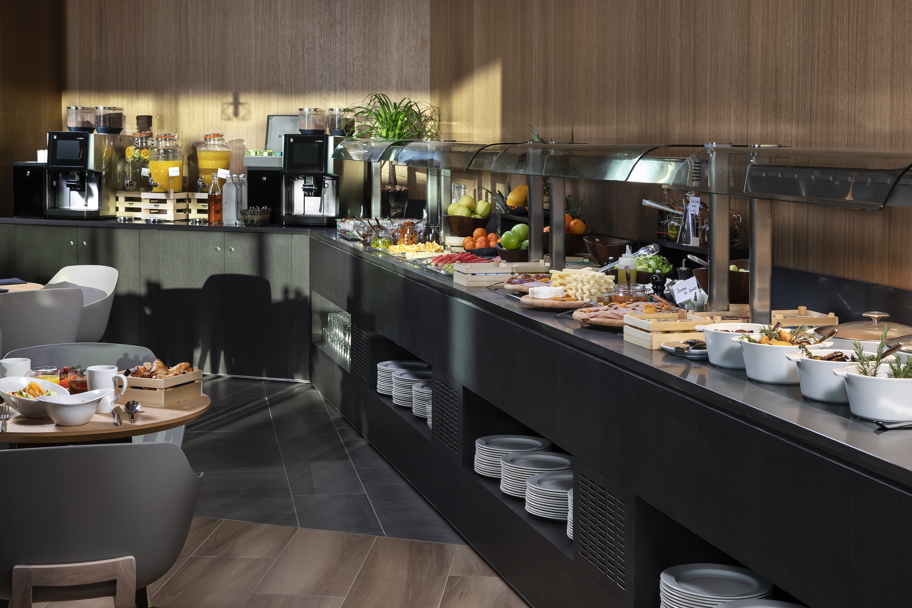 Modern hotel breakfast buffet with fresh fruit, coffee, juice, and hot dishes.