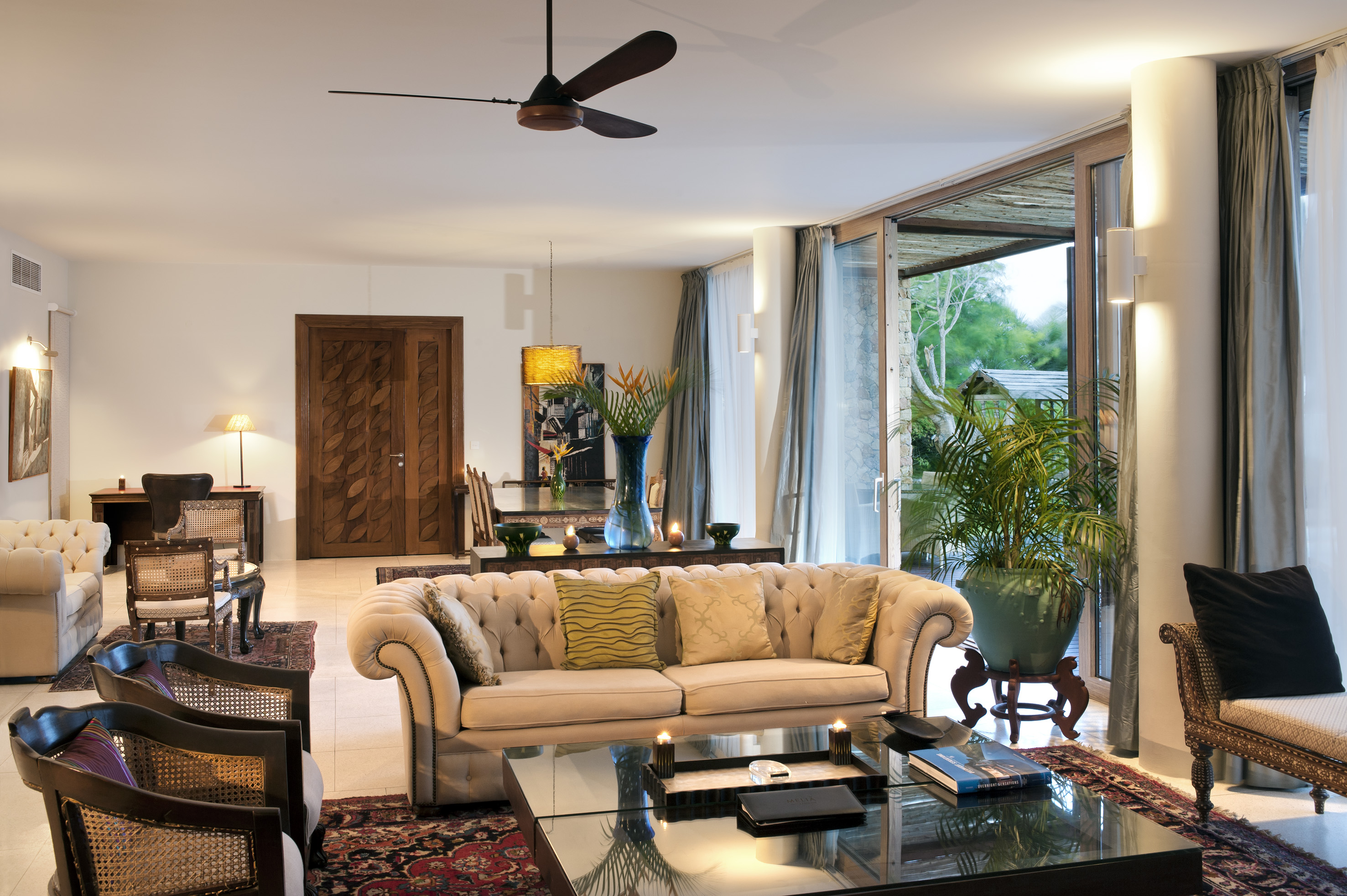 Elegant living room: tufted sofa, wood furniture, glass table, tropical view.