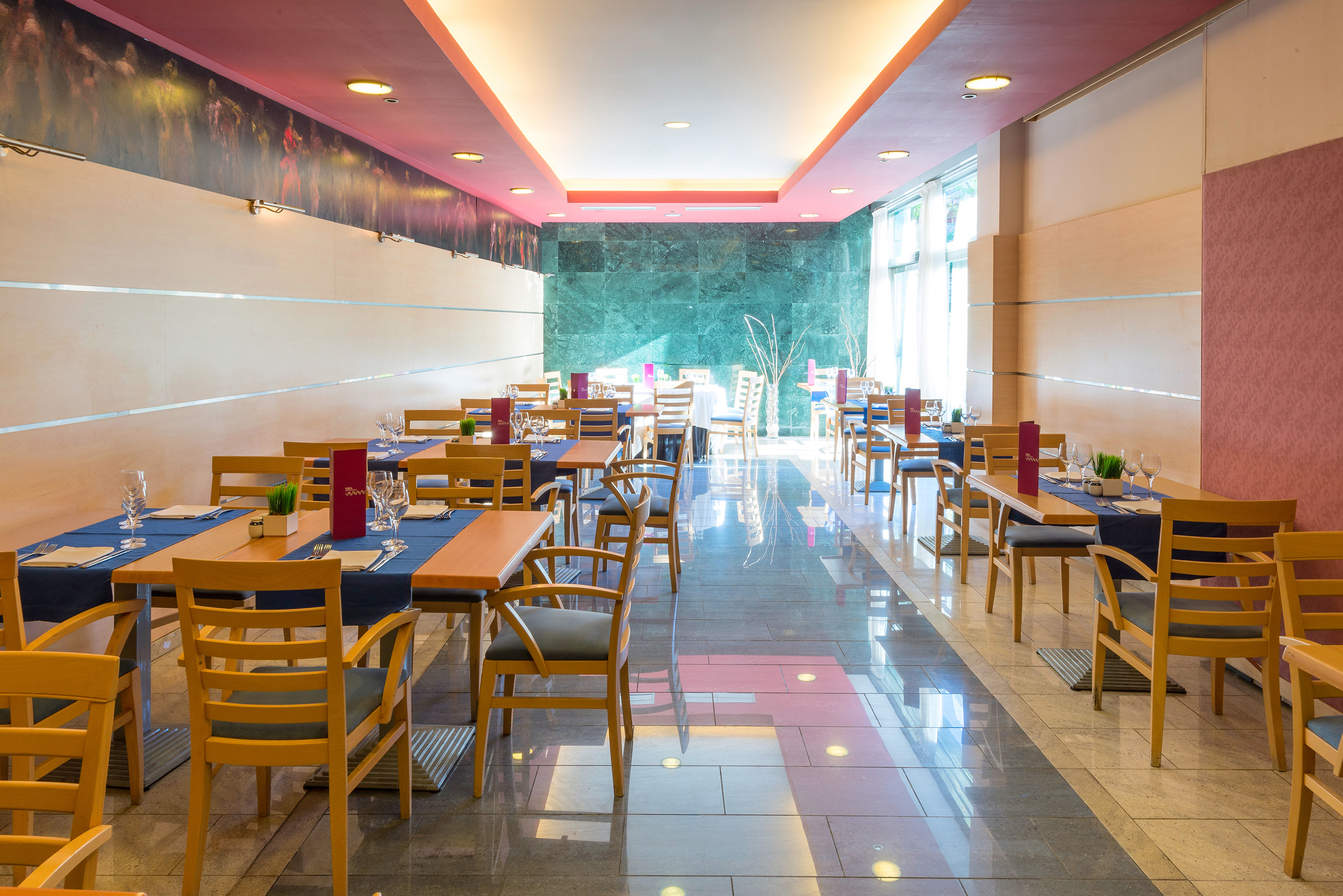 Bright, modern restaurant dining room with set tables and wooden chairs.
