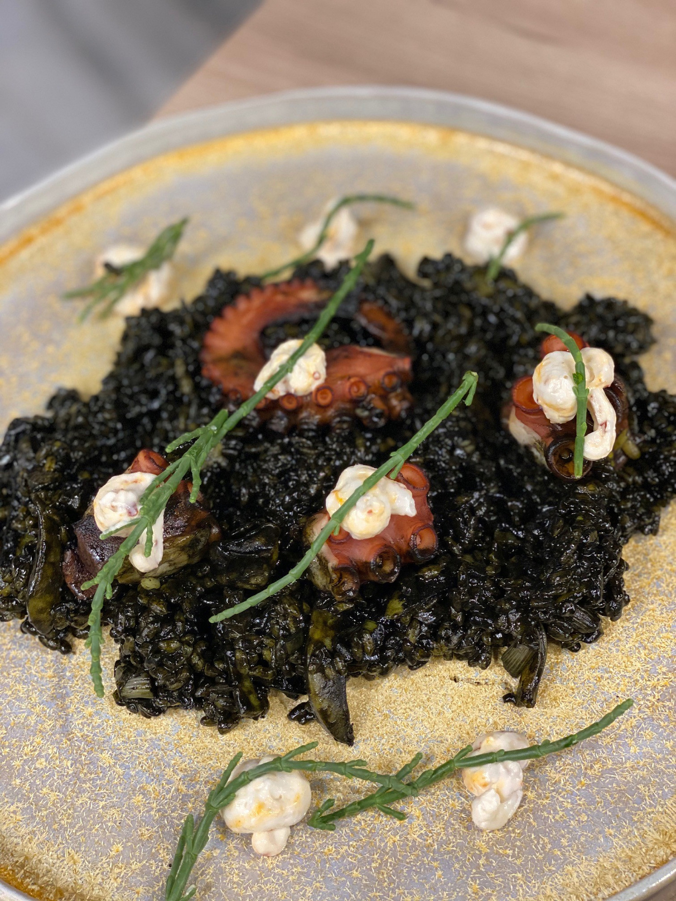 Black squid ink rice with grilled octopus, aioli, and samphire garnish.