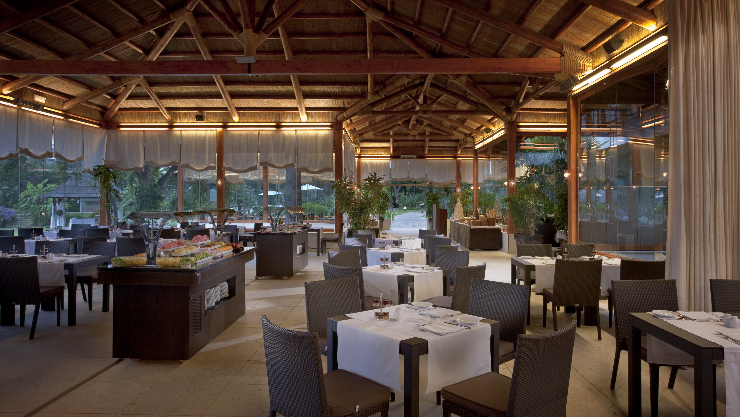 Elegant resort restaurant with thatched roof, buffet, and garden view.