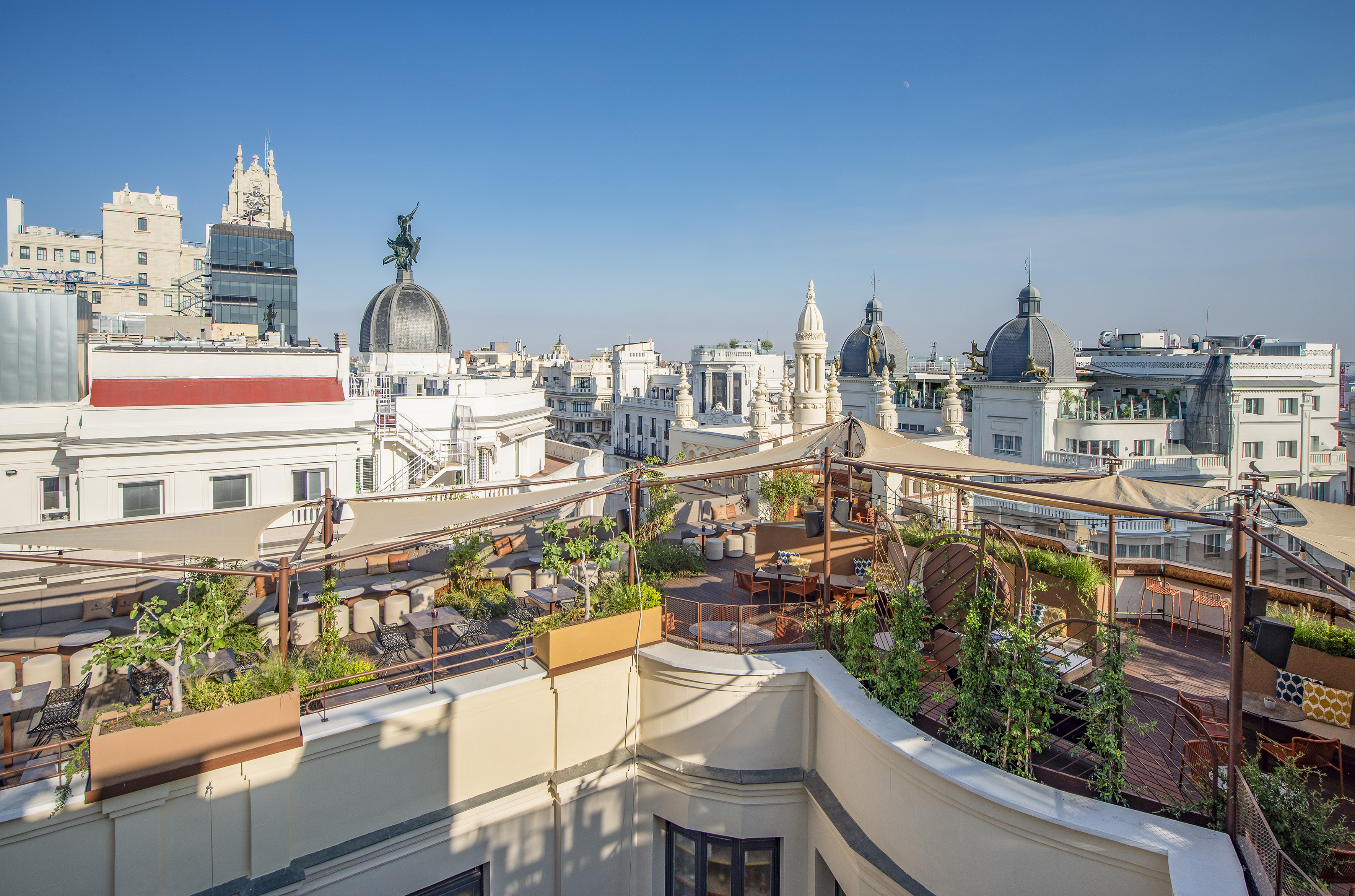 Sunny Madrid rooftop terrace with outdoor seating, plants, and historic city skyline.