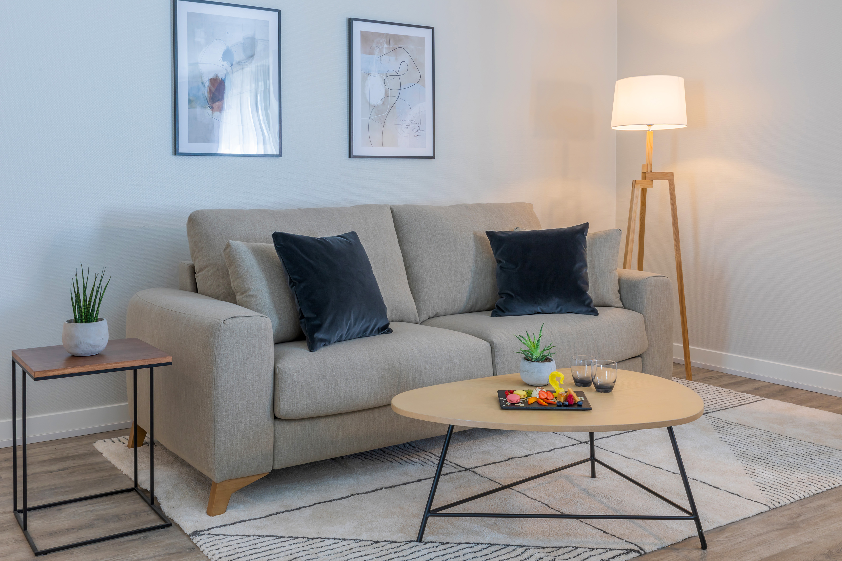 Modern living room with beige sofa, wooden coffee table, floor lamp, abstract art.
