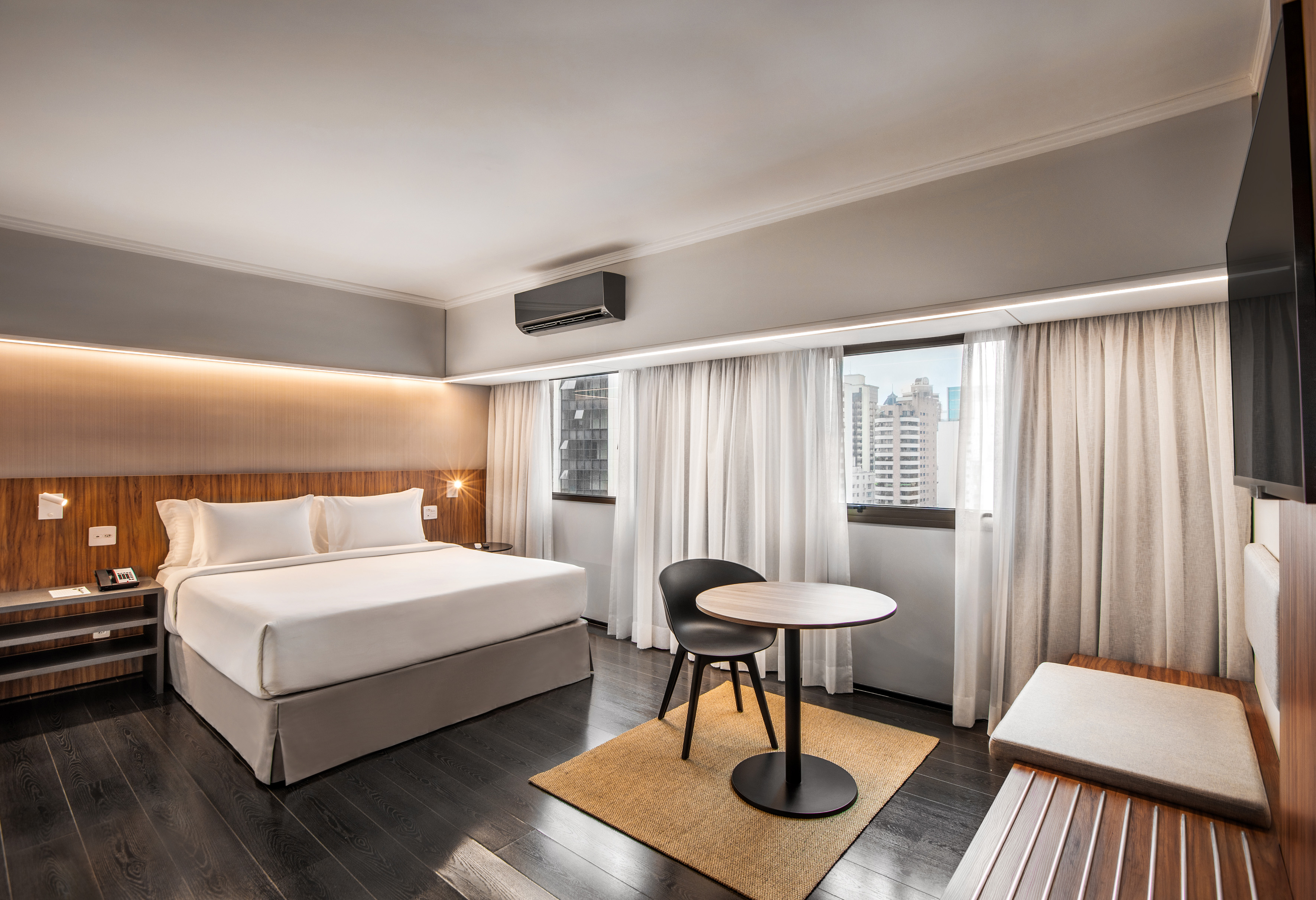 Spacious modern hotel room with king bed, city view, dark wood floor, and seating.