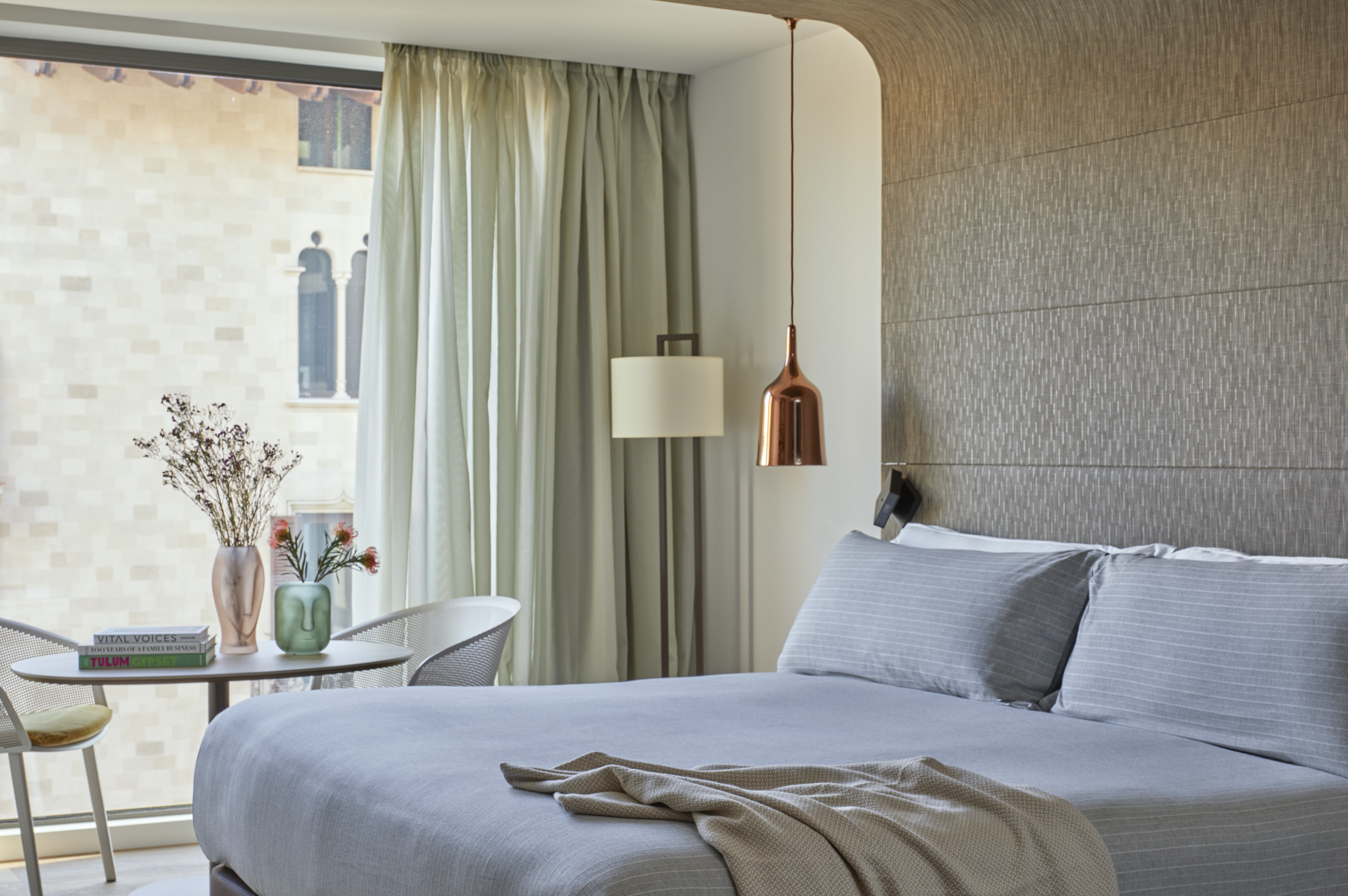 Stylish modern bedroom with grey bed, city view window, and minimalist decor.