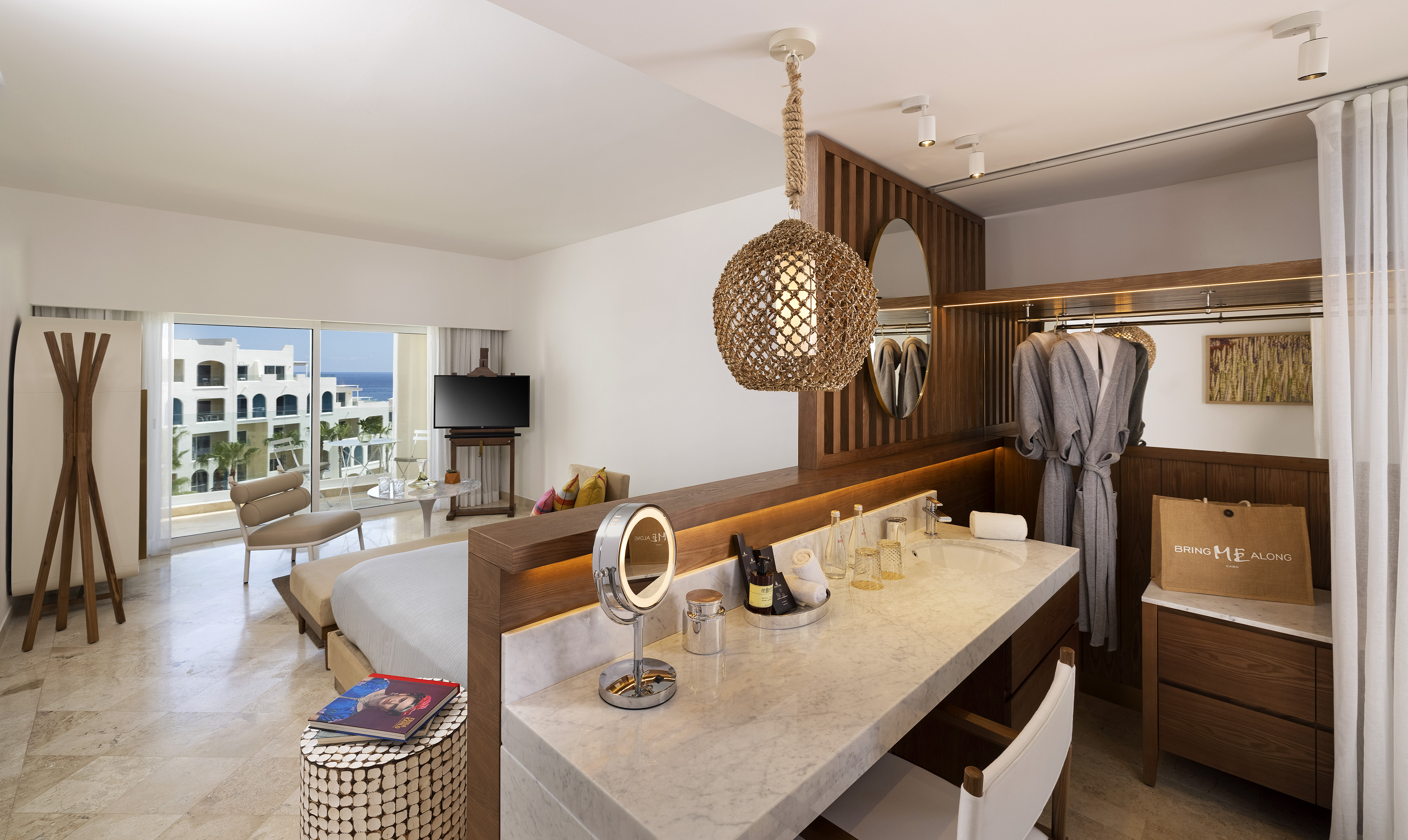 Modern resort suite with ocean view, bedroom, and vanity bathroom.