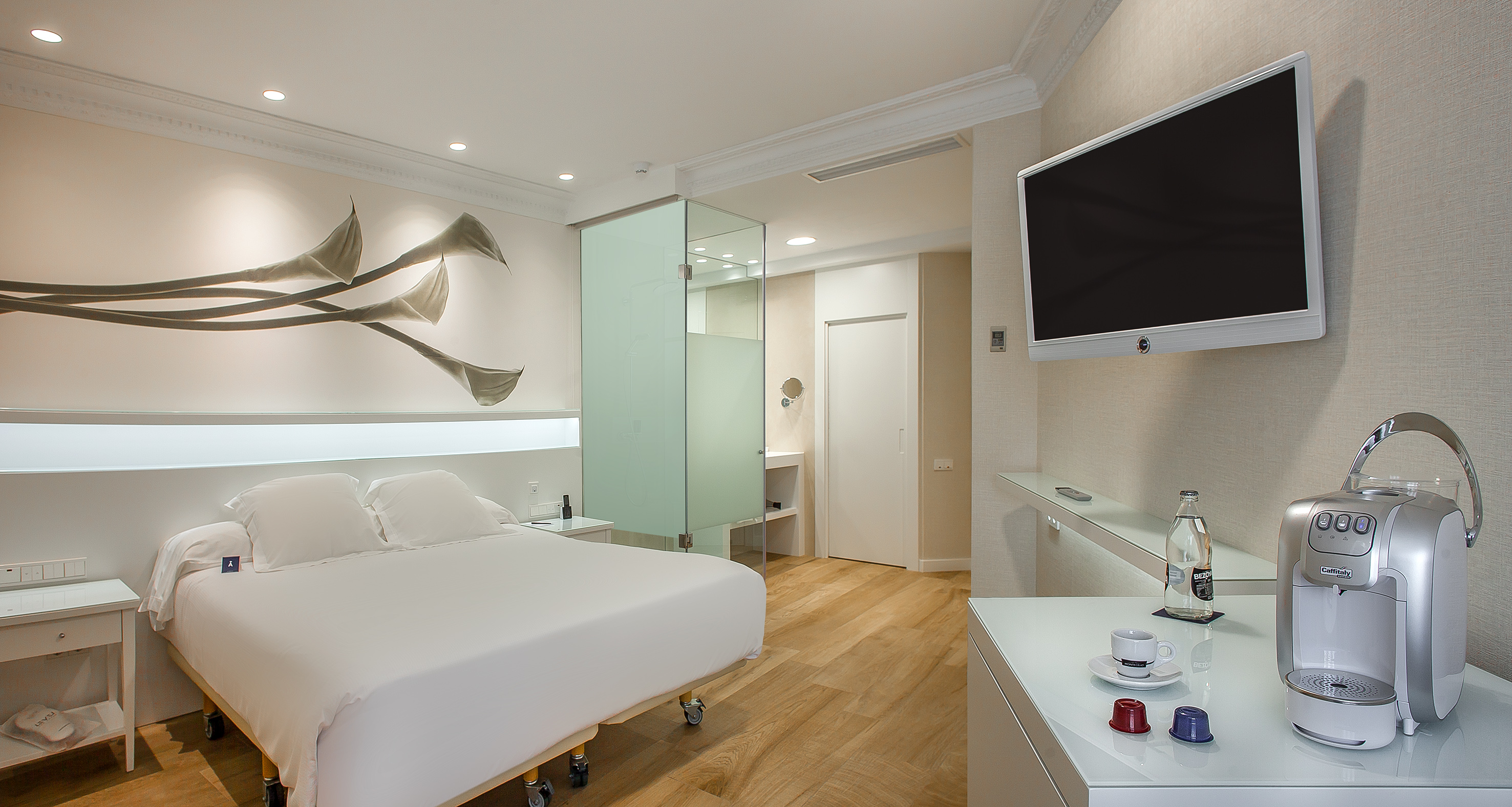 Modern hotel room with white bed, stylish wall art, TV, and coffee maker.