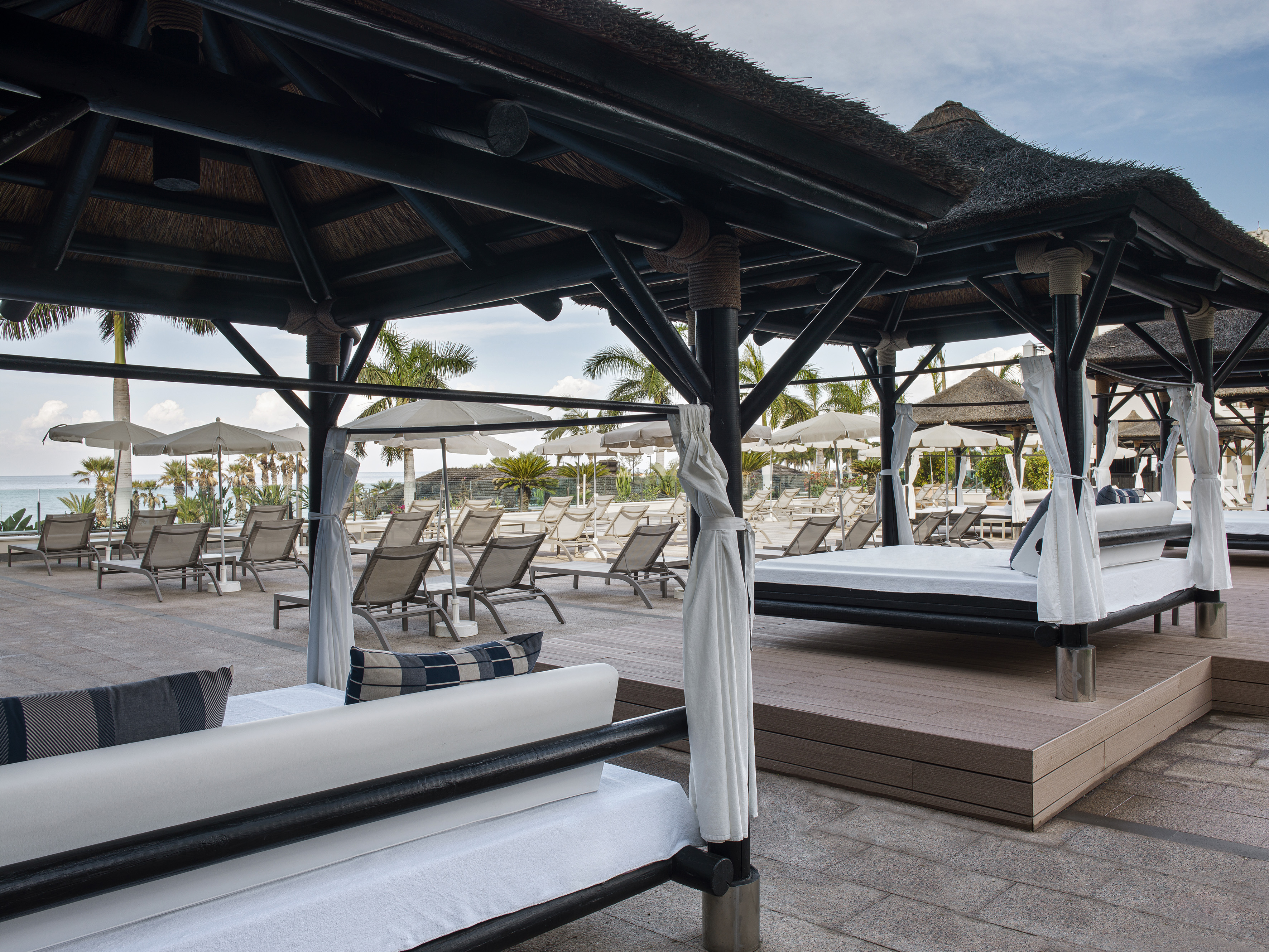 Luxury resort thatched cabanas with white daybeds by the ocean.