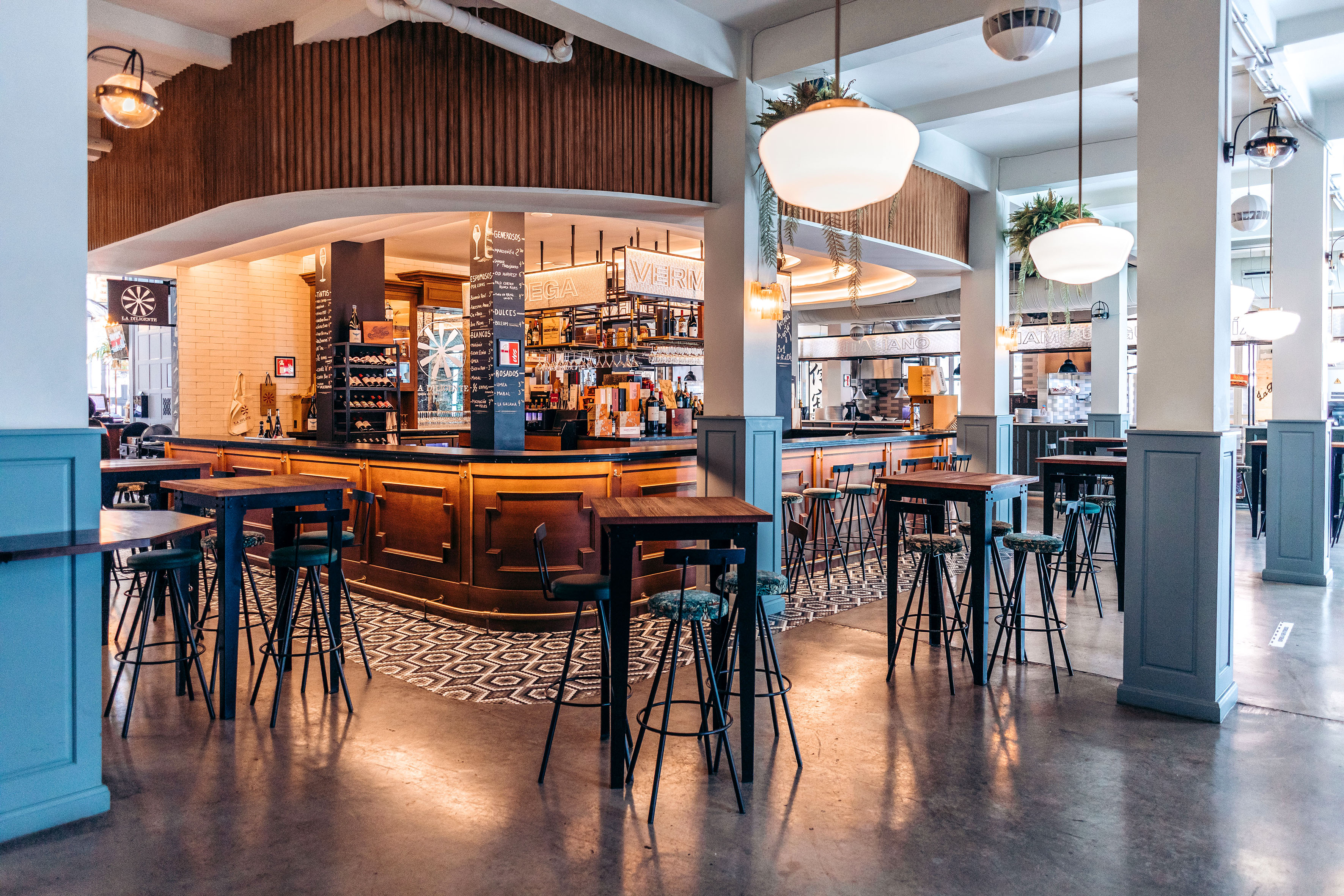 Modern bar interior with a wooden counter, high tables, and bar stools.