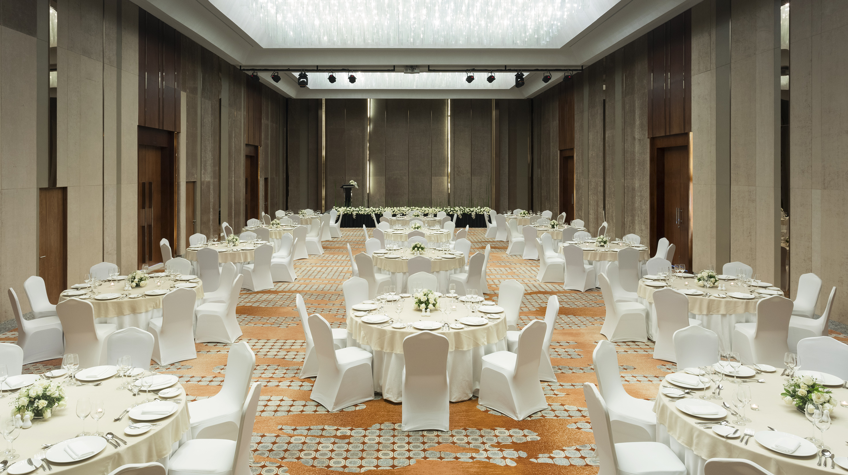 Elegant ballroom with set tables, white chairs, and floral decor for banquet or wedding.