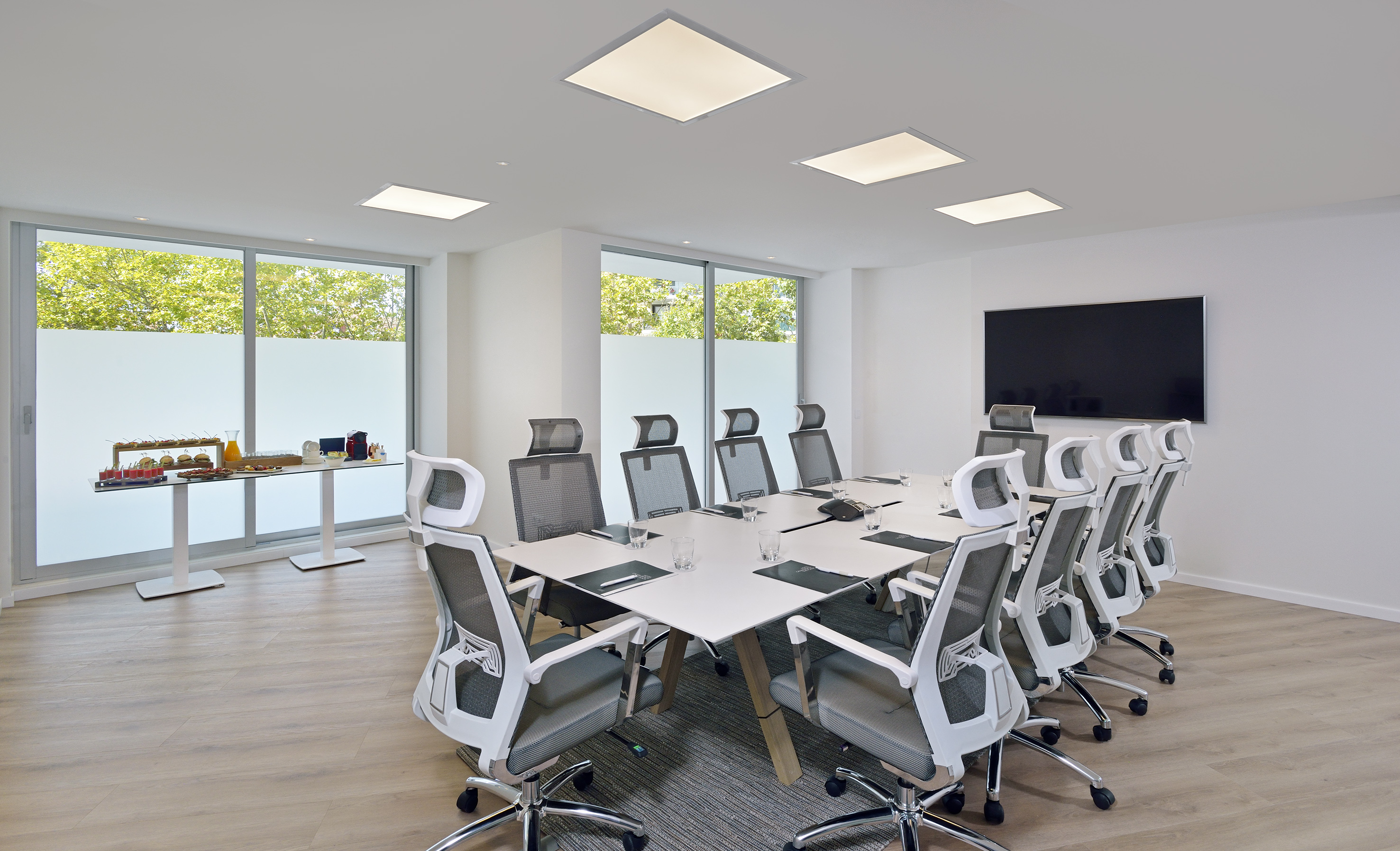 Modern meeting room with large table, office chairs, TV, and catering.