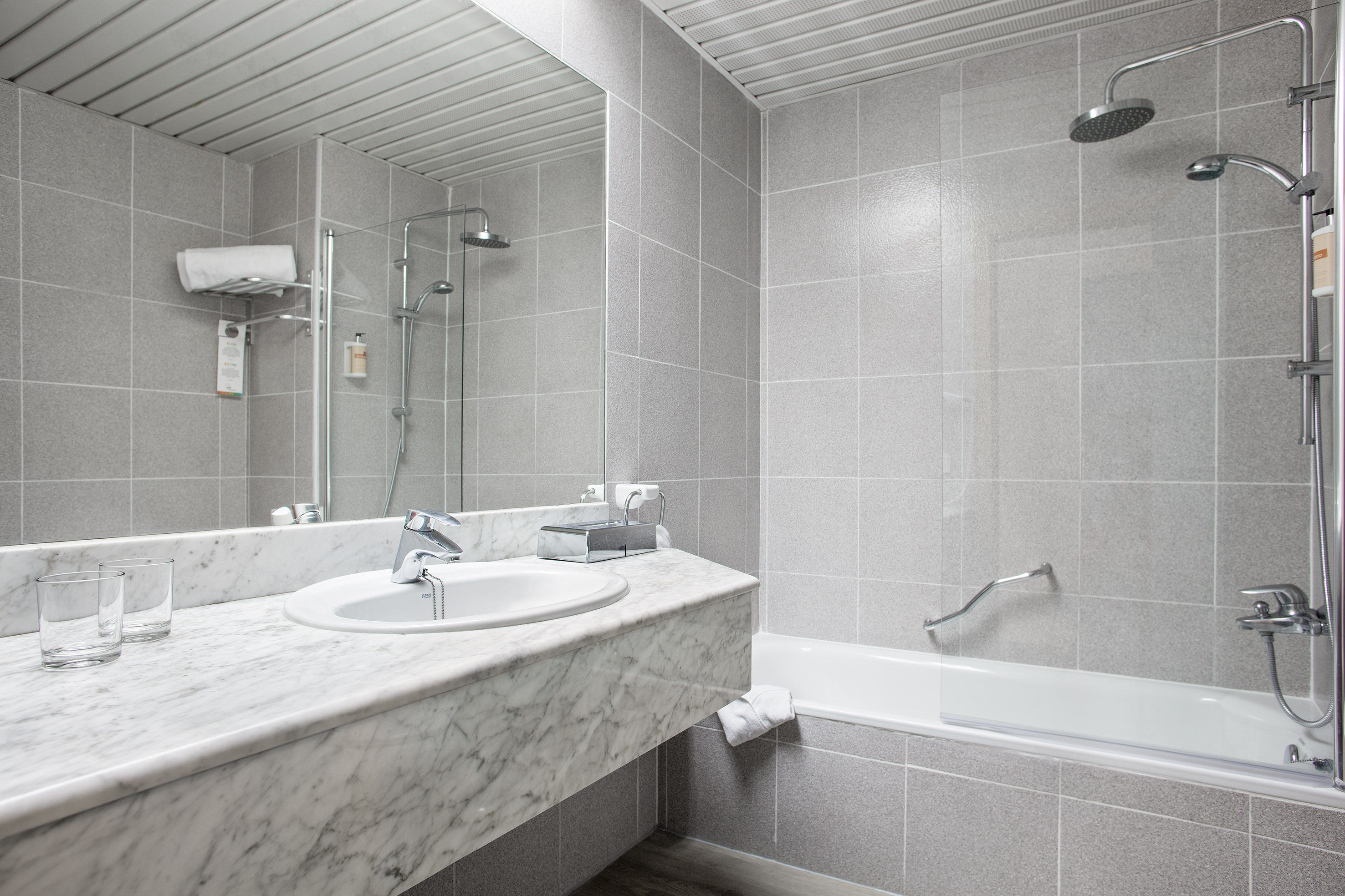 Gray tiled hotel bathroom with marble vanity, sink, mirror, and shower bathtub.