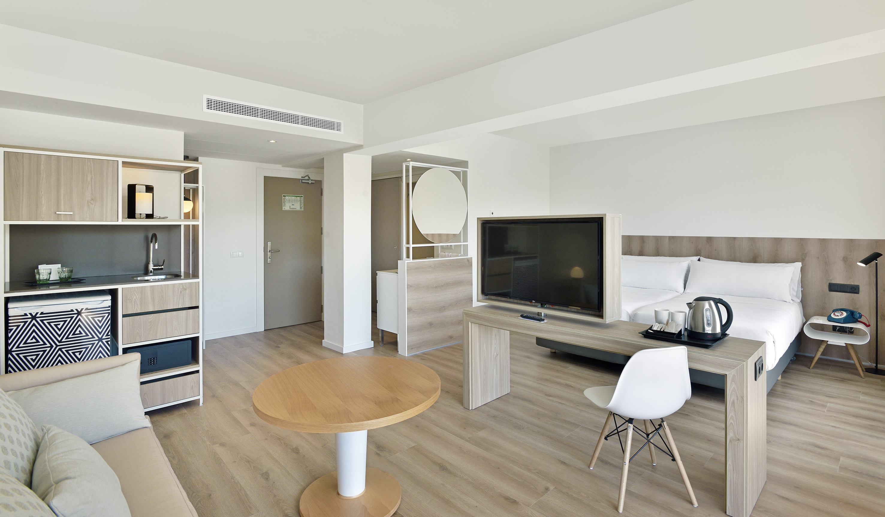 Minimalist hotel studio apartment with kitchenette, bed, TV, and lounge area.