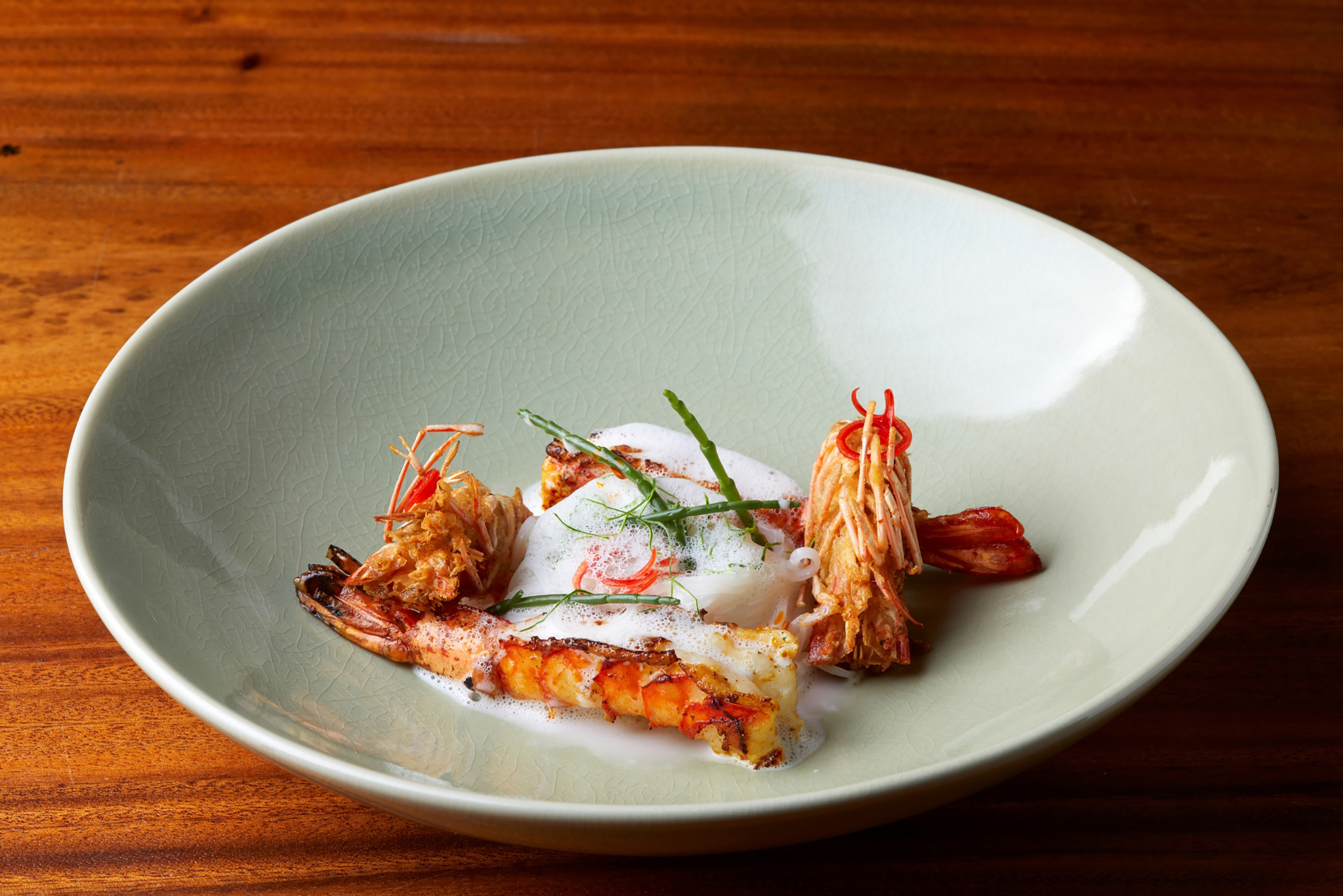 Seared prawns with foam, sea beans, and chili on a crackled green plate.