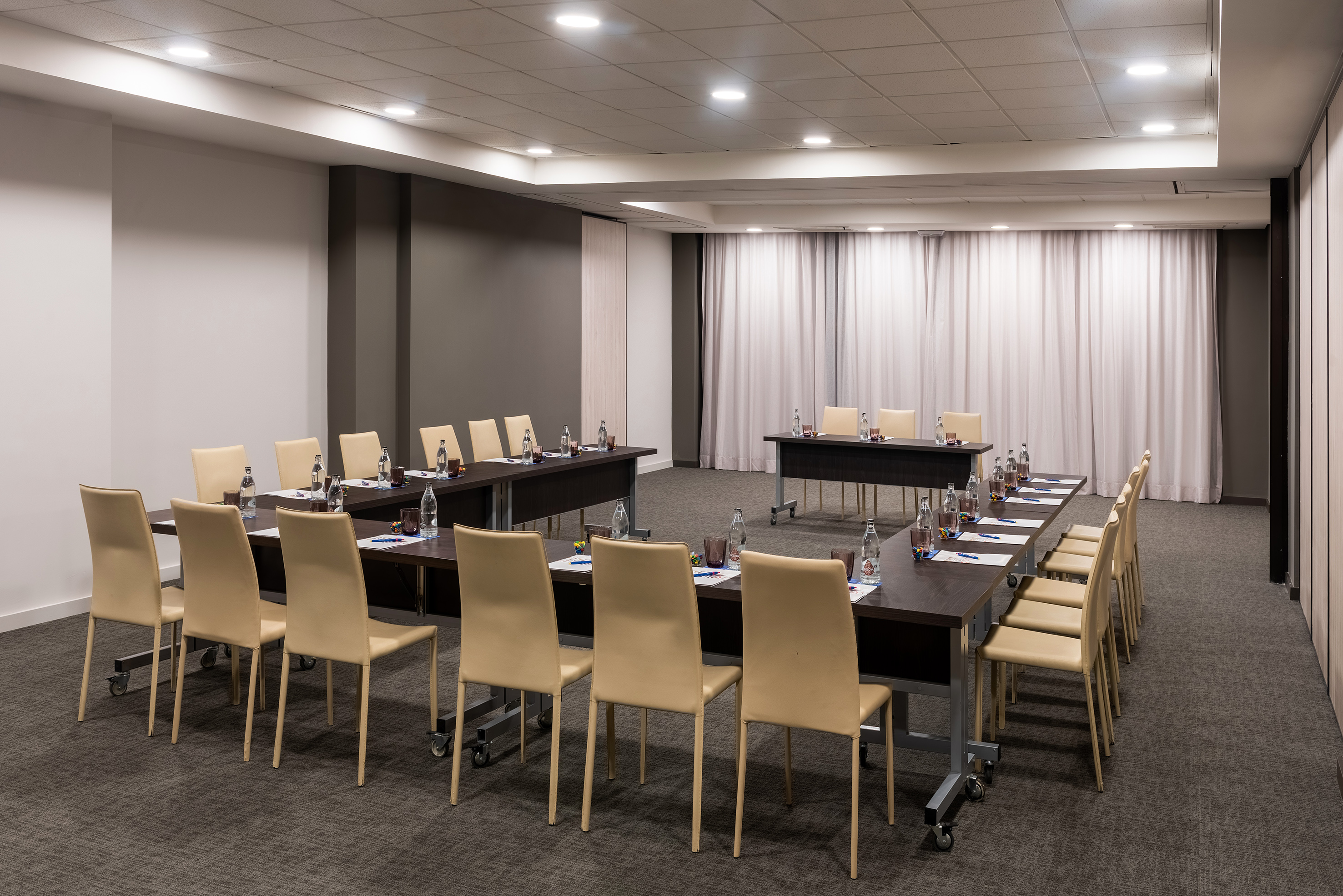 Modern conference room with U-shaped table, beige chairs, and bottled water.