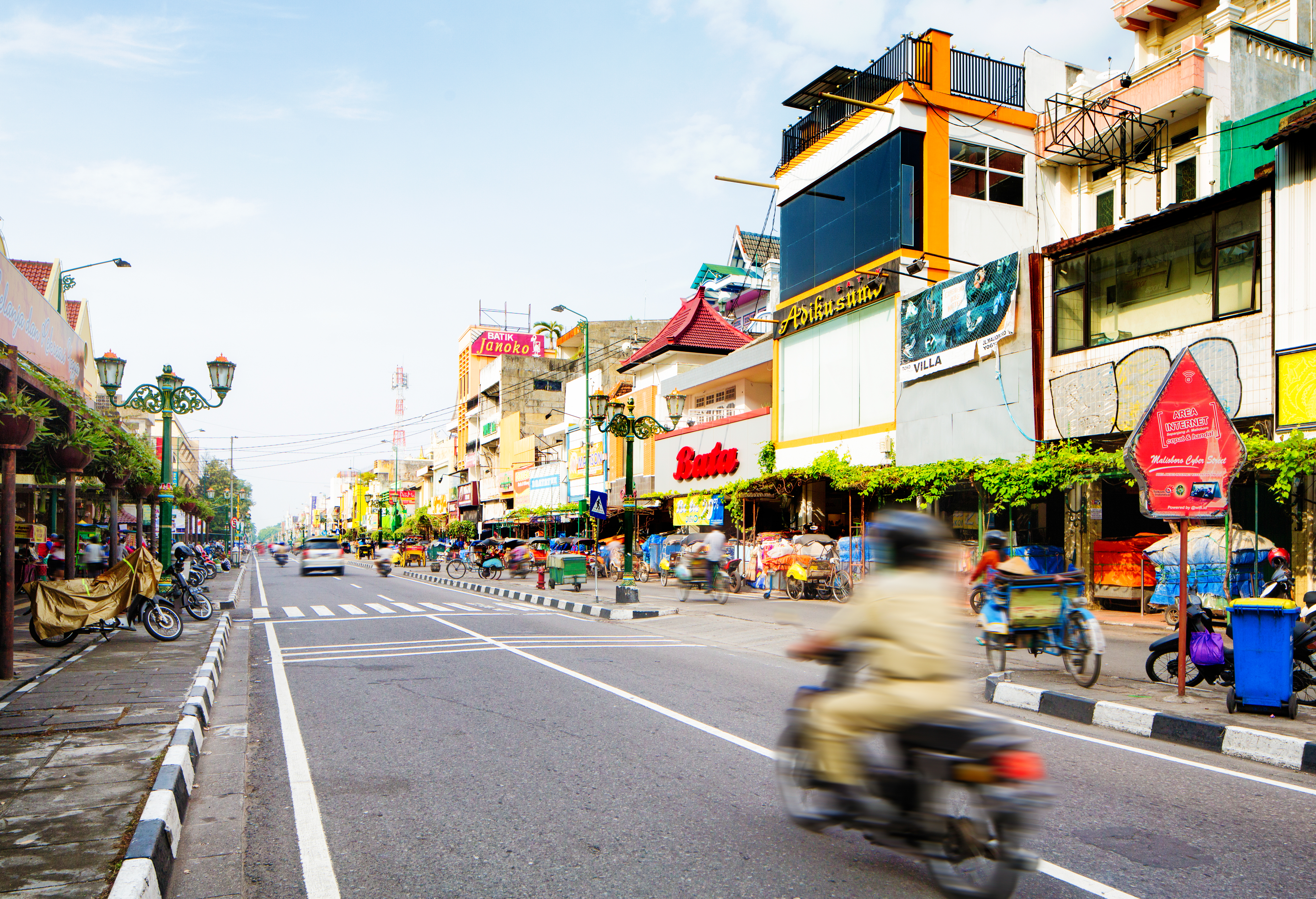 Busy Malioboro streetscape with shops, motorcycles, and becak in Yogyakarta.