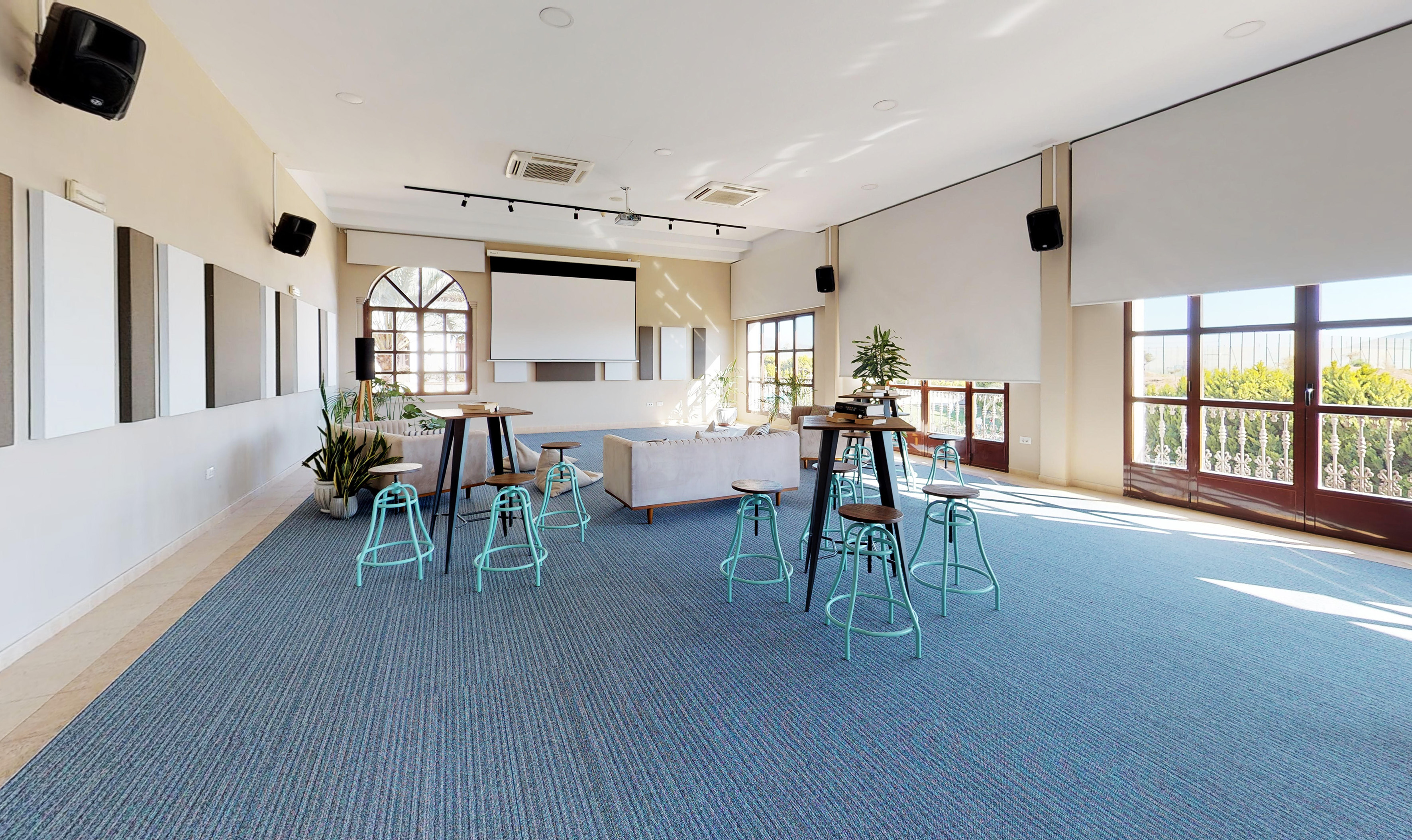 Versatile event space with blue carpet, projector, lounge, and high tables.