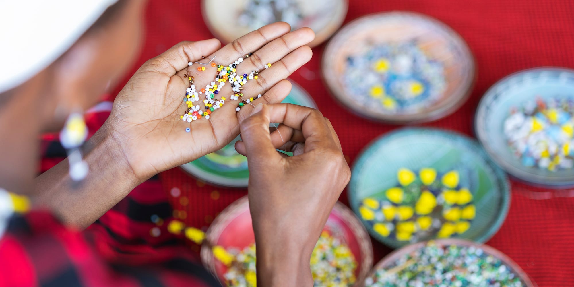 Artisan hands beading colorful small beads for jewelry craft.