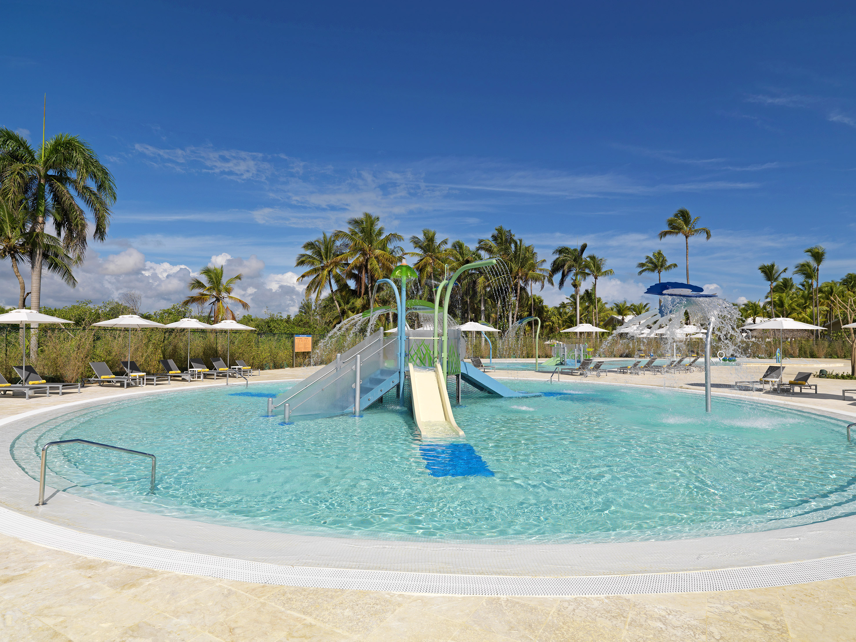 Family-friendly resort splash pad with water slides, sprinklers, and palm trees.