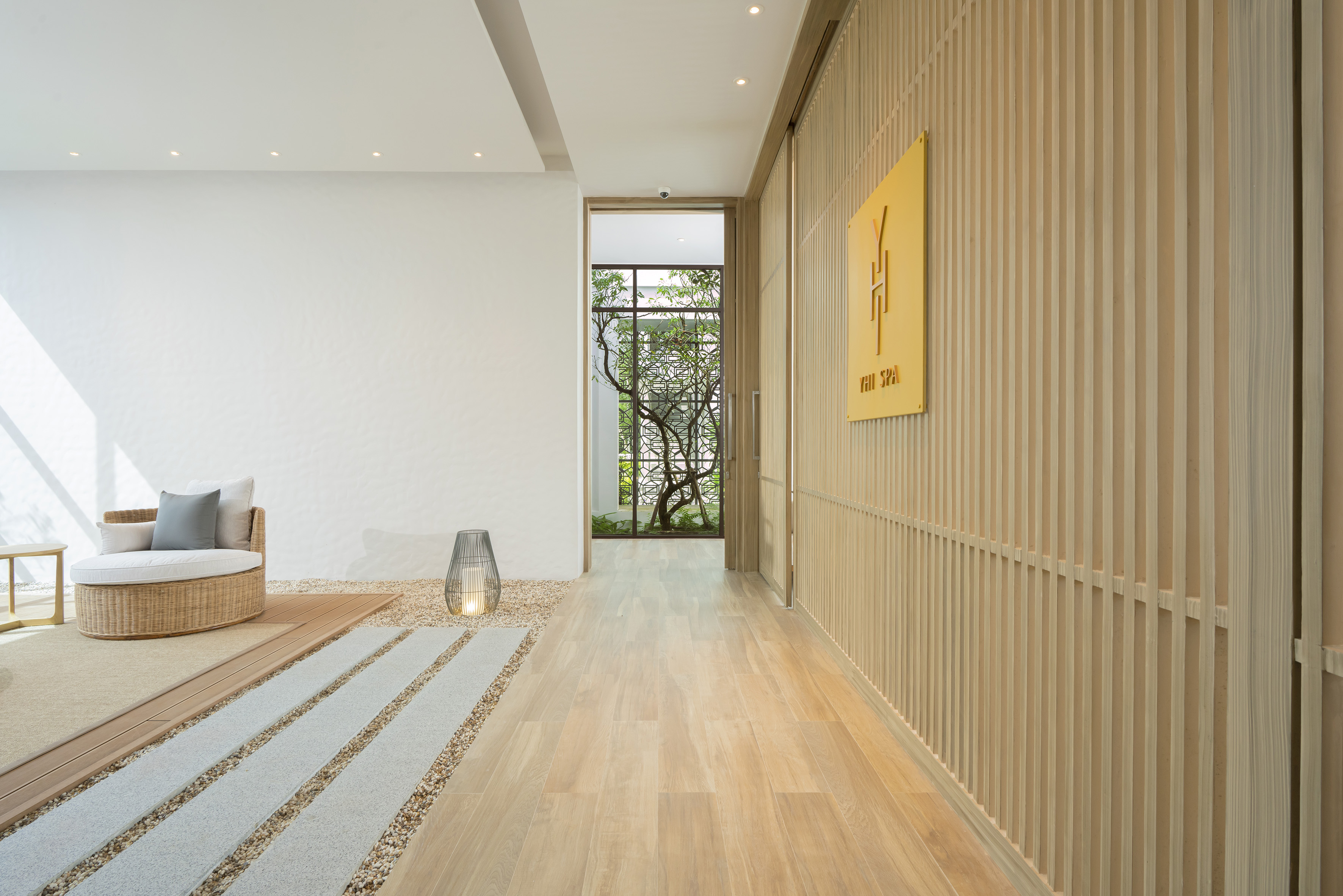 YHI SPA waiting area: light wood, slatted wall, wicker chair, garden view.