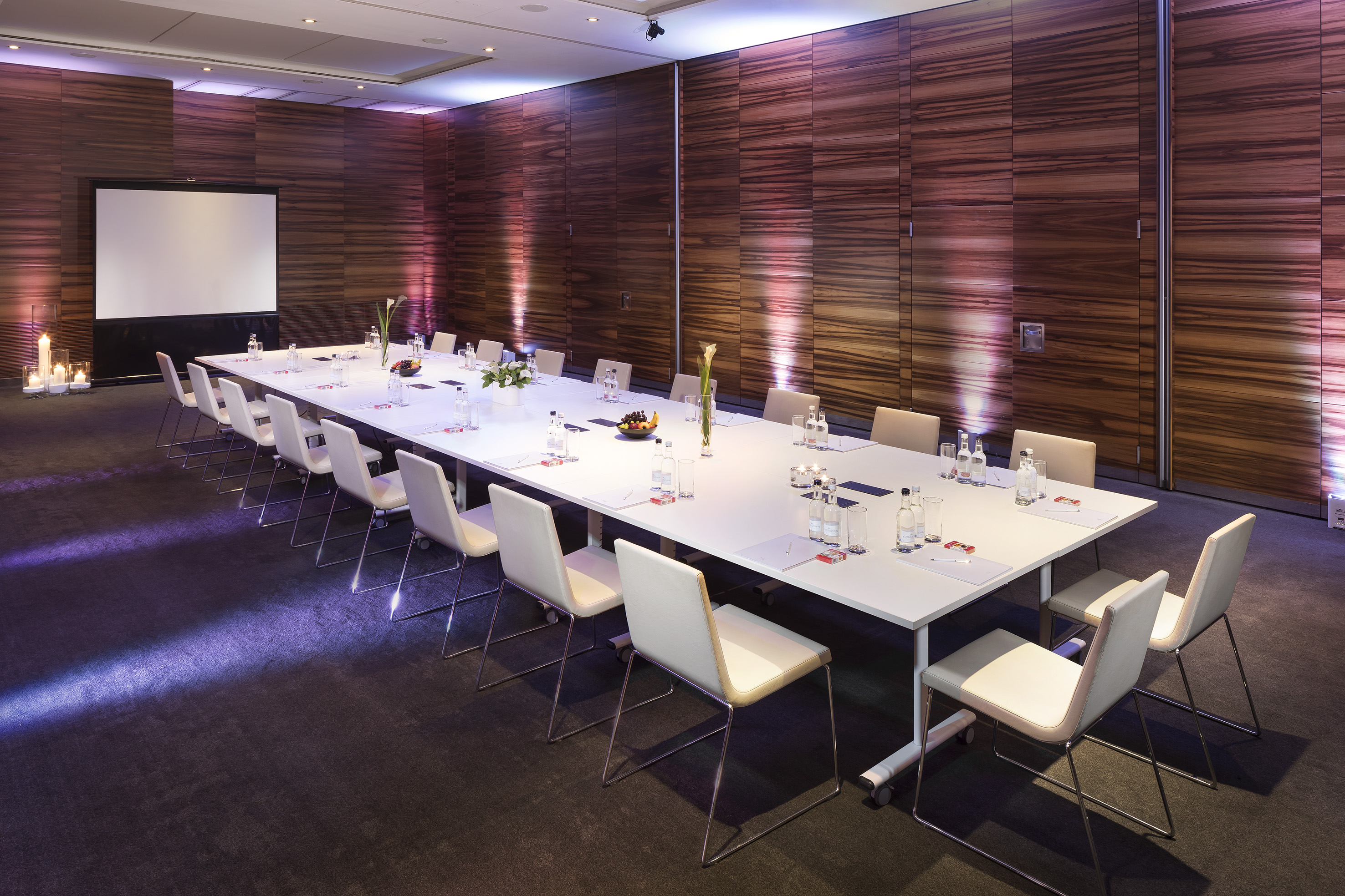 Modern conference room with white table, chairs, projection screen, and wood walls.